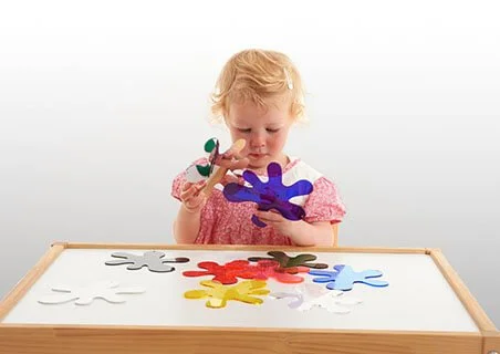 A young girl playing with colorful paper cutouts on a table.