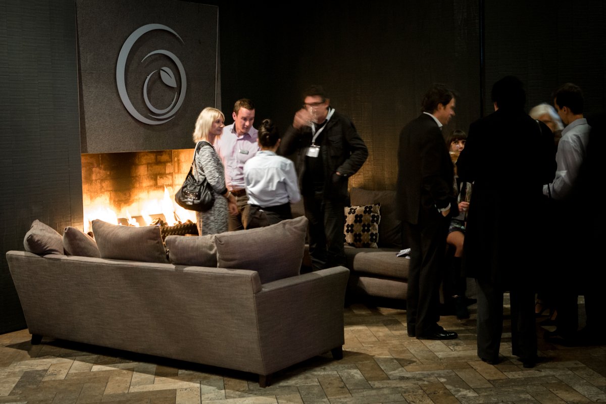 Group of people socializing in a modern lounge with a fireplace and dark walls.
