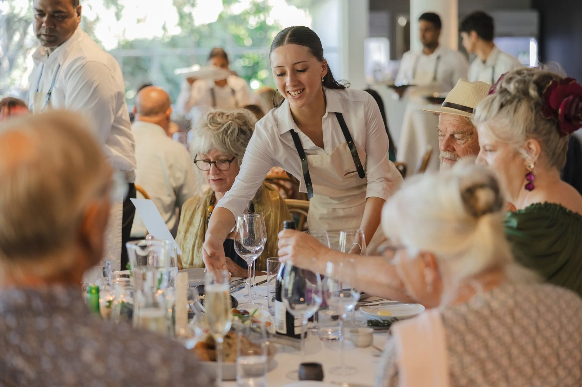 A young waitress serving elderly guests at a restaurant during daytime