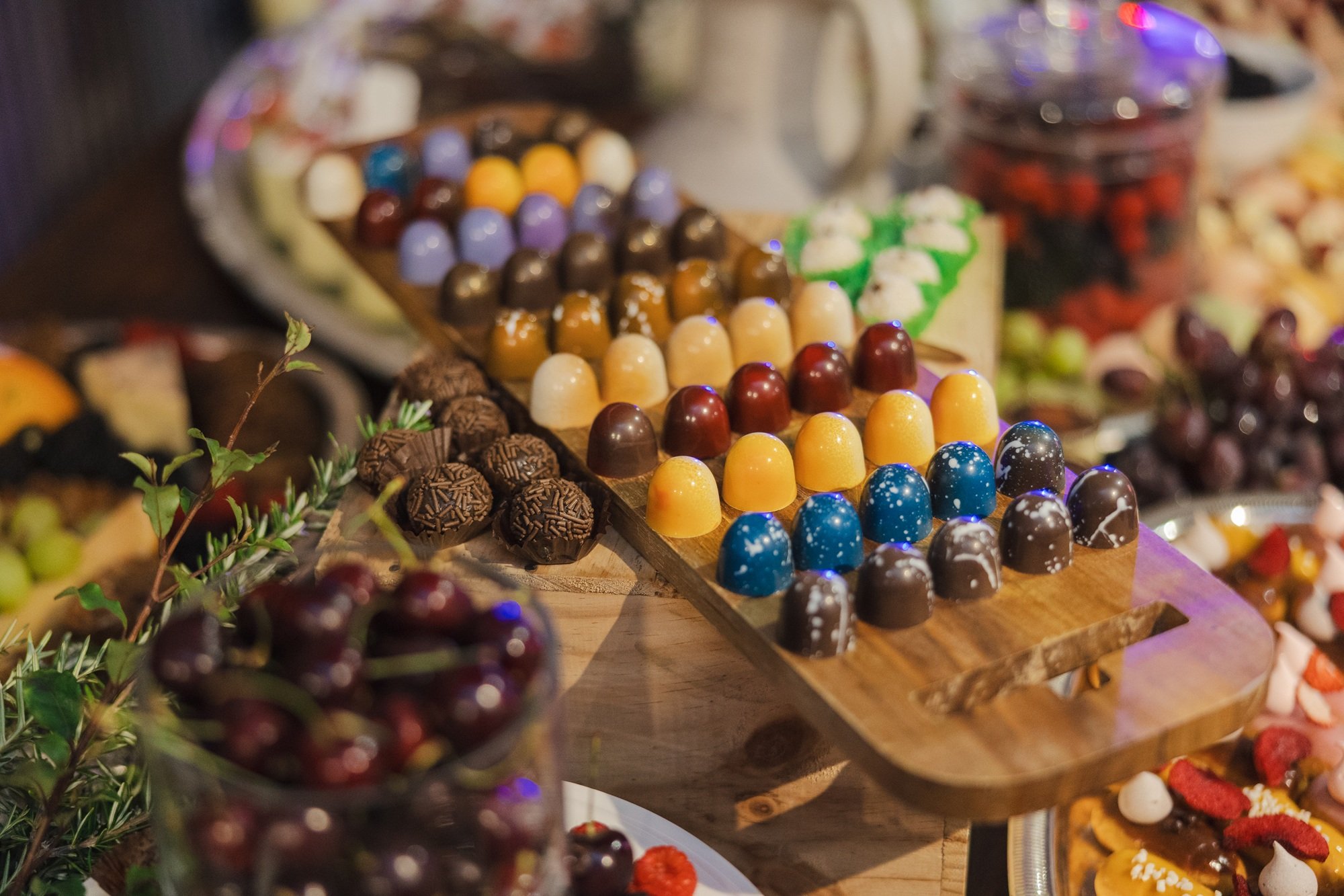 Assorted colorful chocolates displayed on a wooden tray at a dessert table.