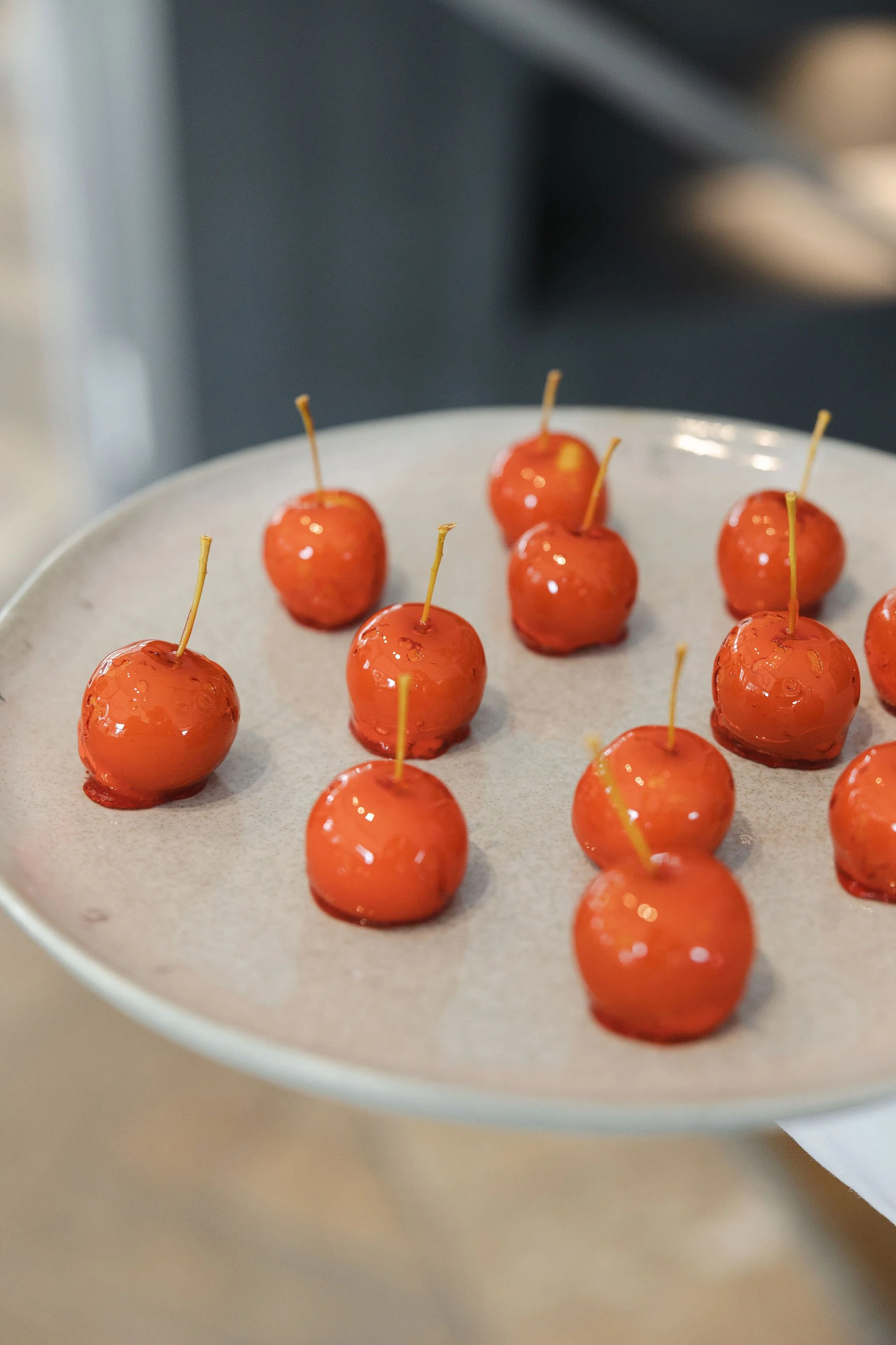 Caramel apples with sticks on a ceramic plate.