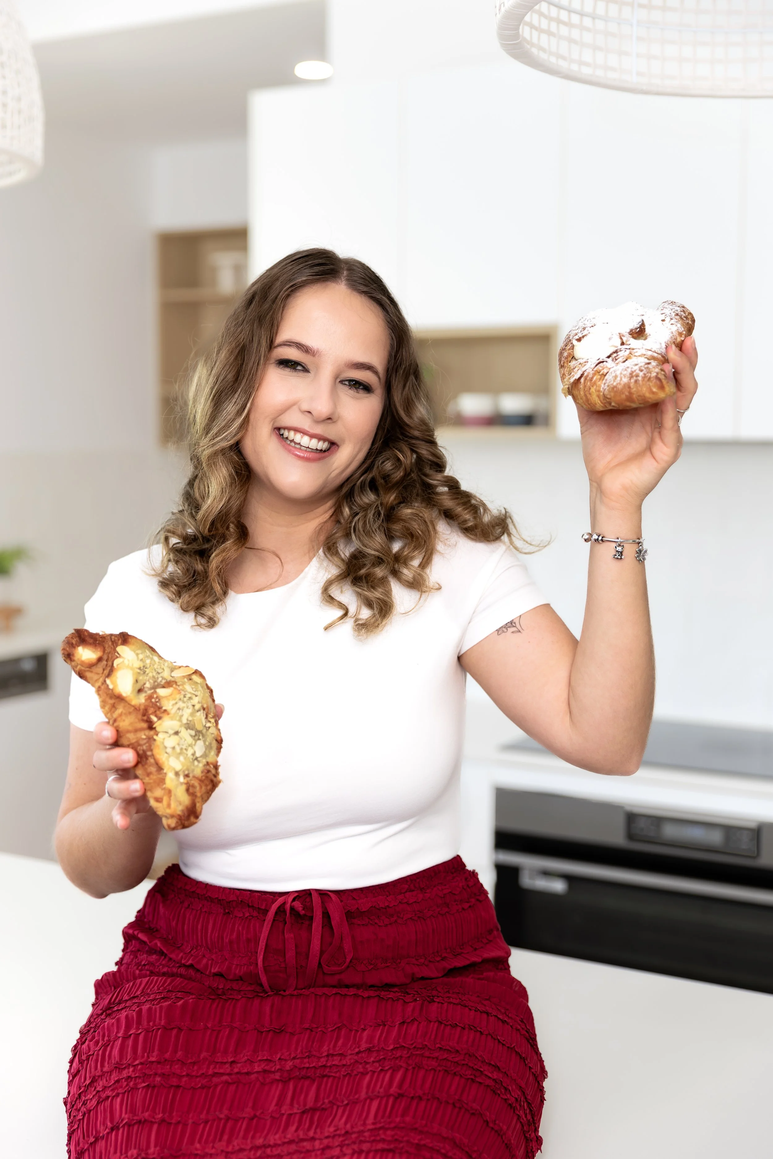 A woman smiling and holding two large pastries in a modern kitchen.