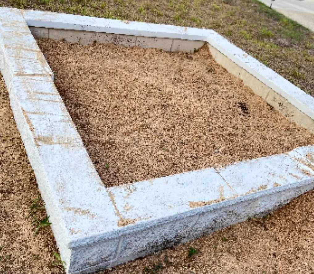 A rectangular border formed with white cinder blocks filled with brown dirt or gravel on the ground.
