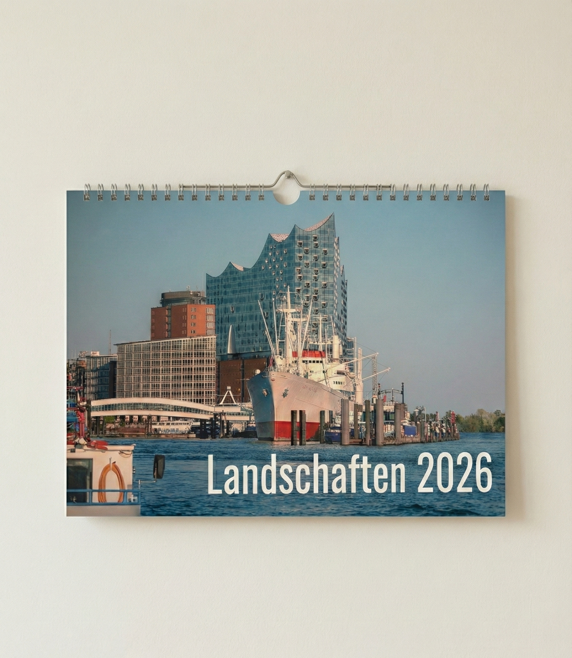 Kalender mit dem Titel 'Landschaften 2026' zeigt ein Modernes Stadtbild mit Hafen, Boot und einem ungewöhnlichen blauen Gebäude, wahrscheinlich in Hamburg.