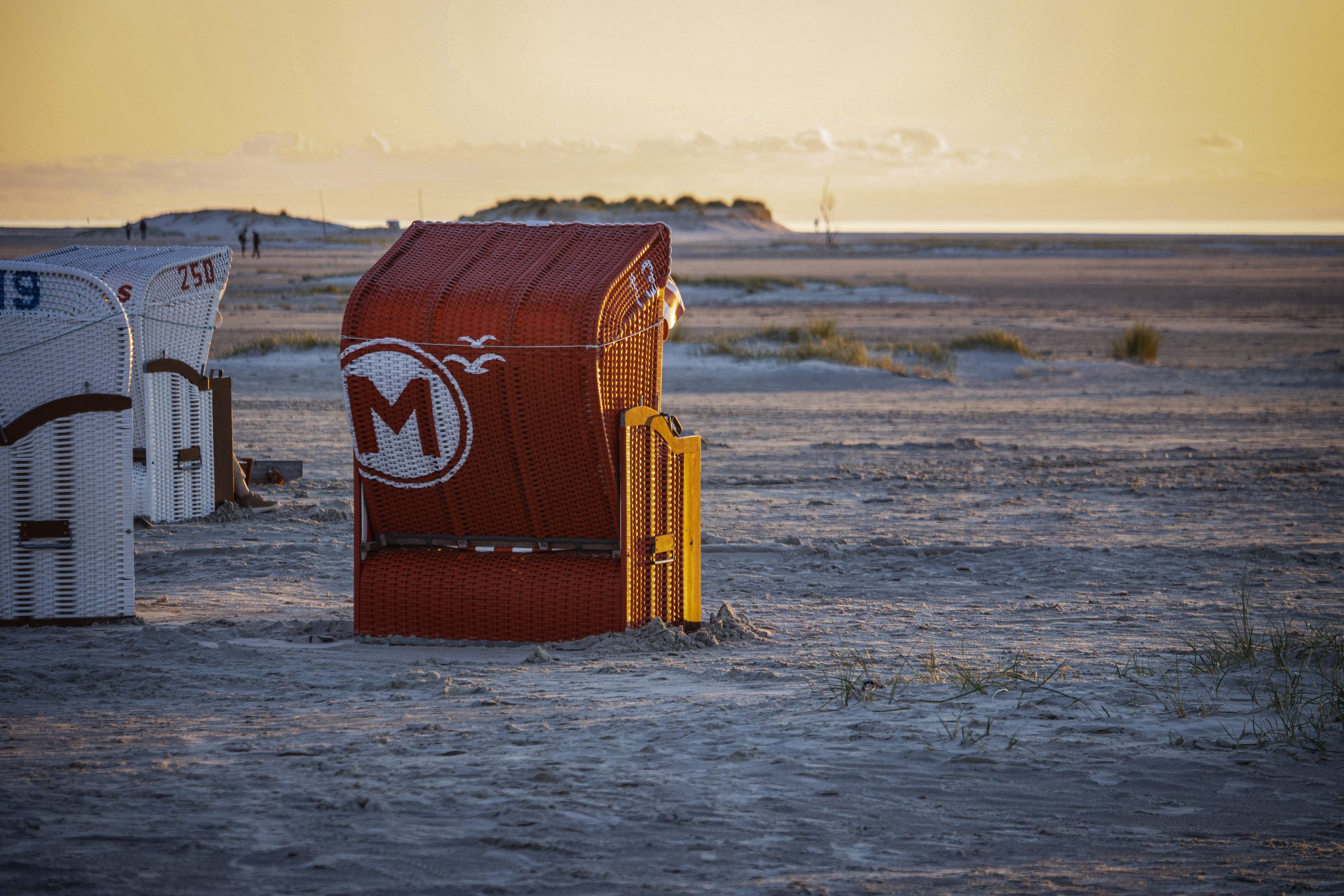 Strand mit Strandkörben, Sonnenuntergang, Sand und wenige Pflanzen