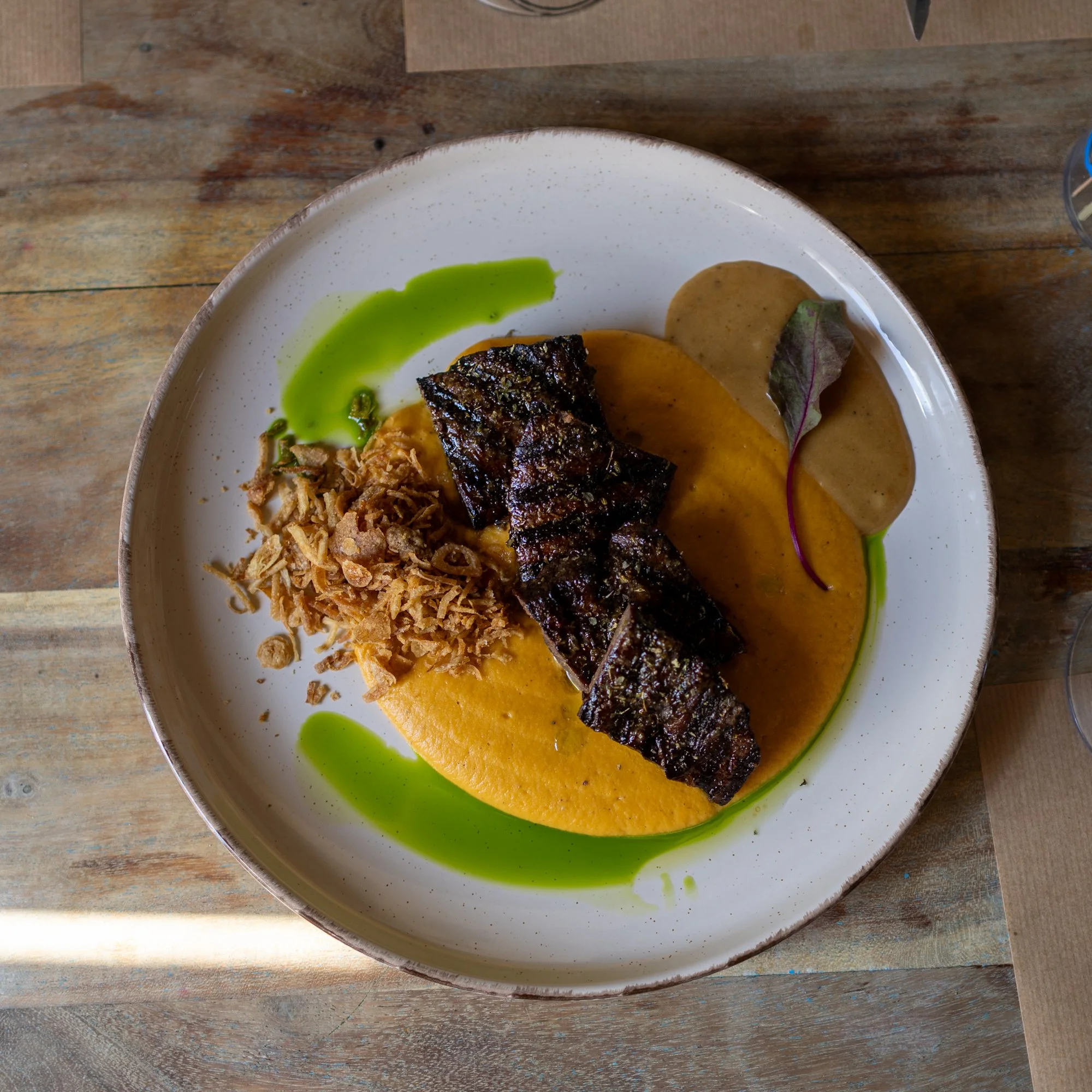 A plated meal with grilled fish on yellow sauce, accompanied by a green sauce, shredded pork, and a purple leaf.