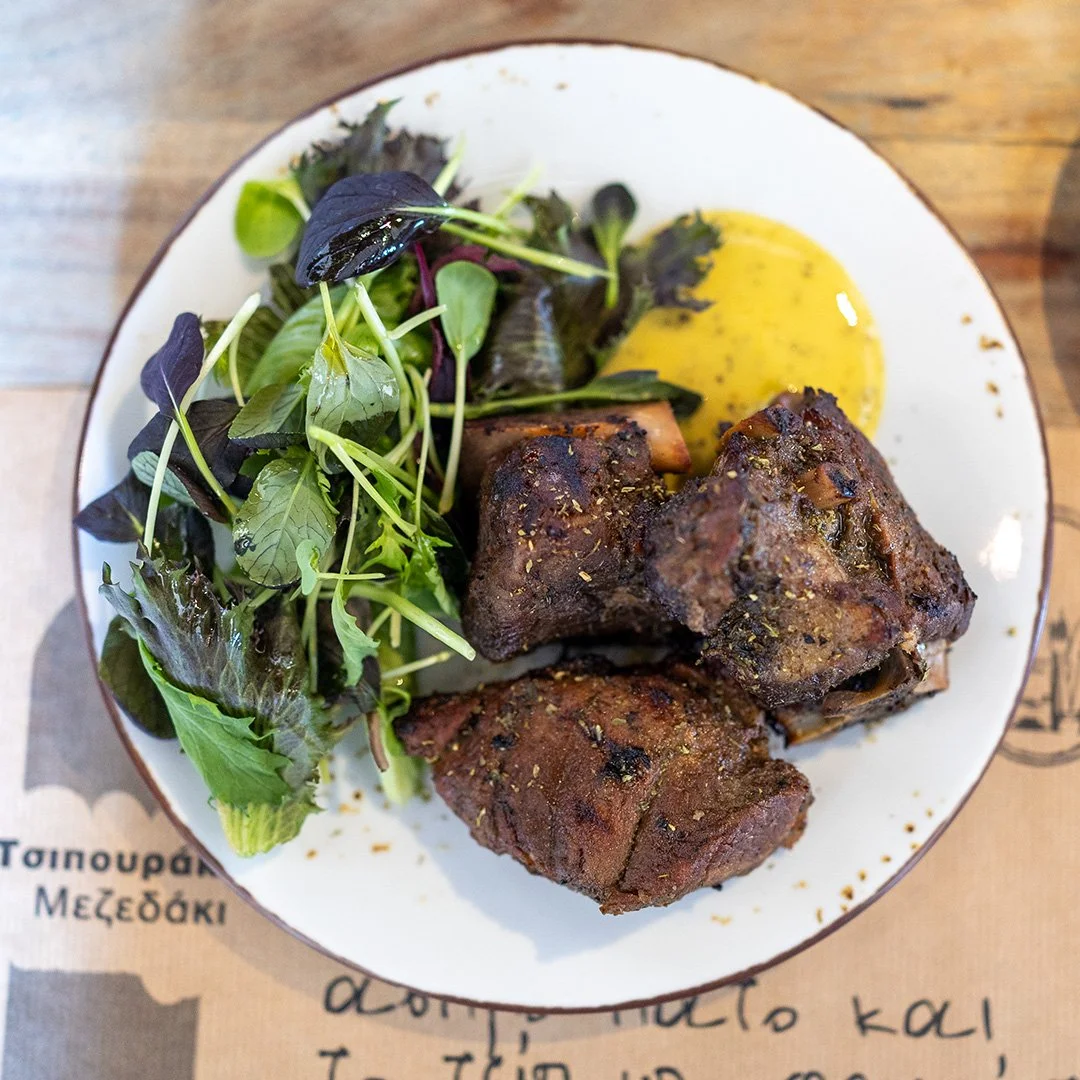 Plate with cooked meat, salad greens, and a yellow sauce or dip on a wooden table.