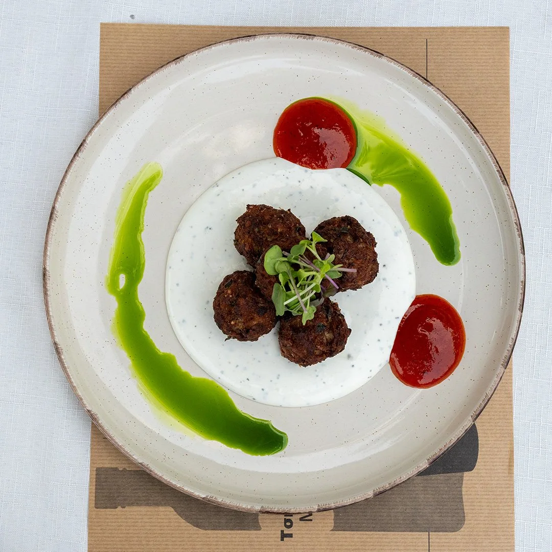 Plate with four falafel balls garnished with microgreens, served with green sauce and two dollops of red sauce on the side.