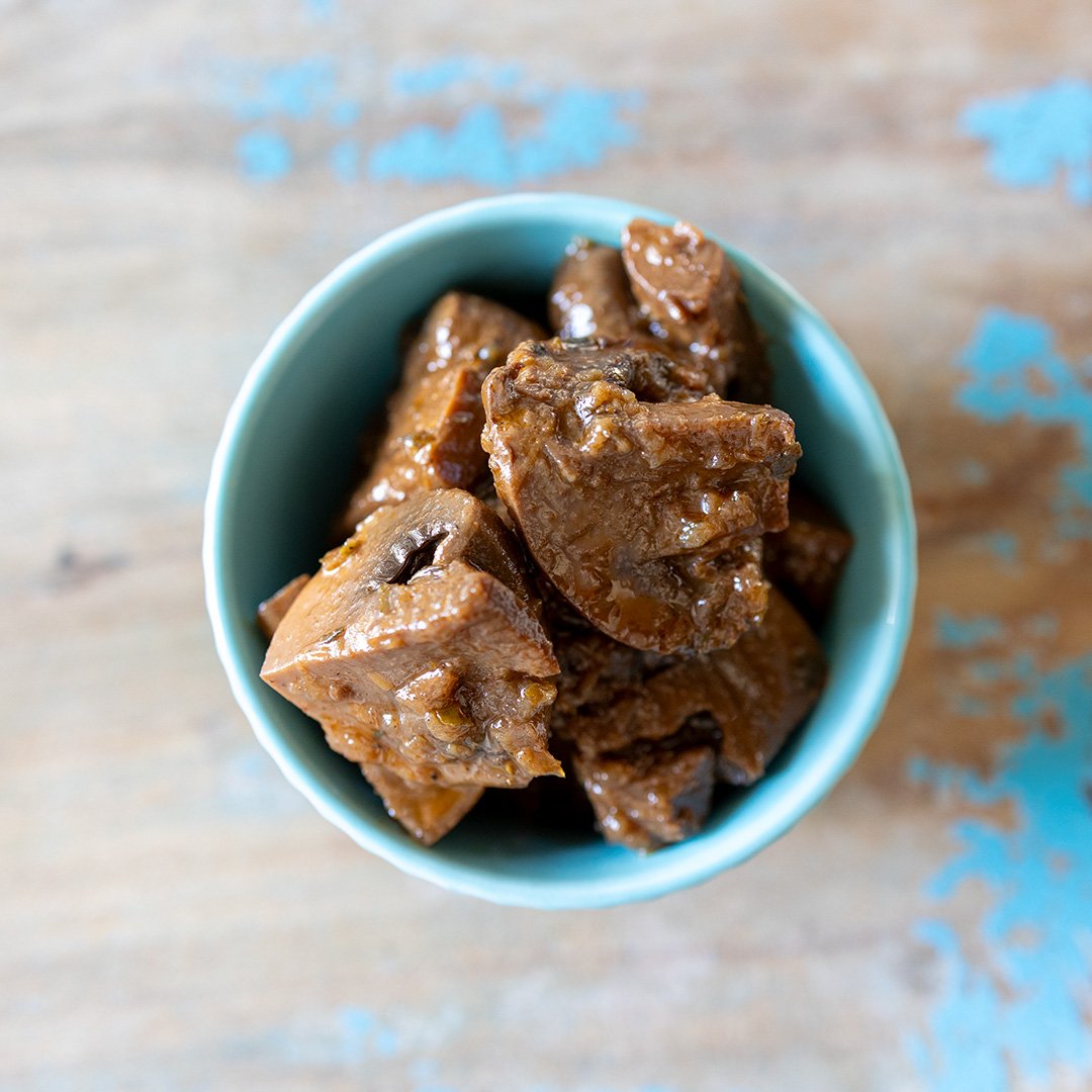 Close-up of a blue bowl filled with cooked beef chunks in gravy on a wooden table with blue paint splatters.