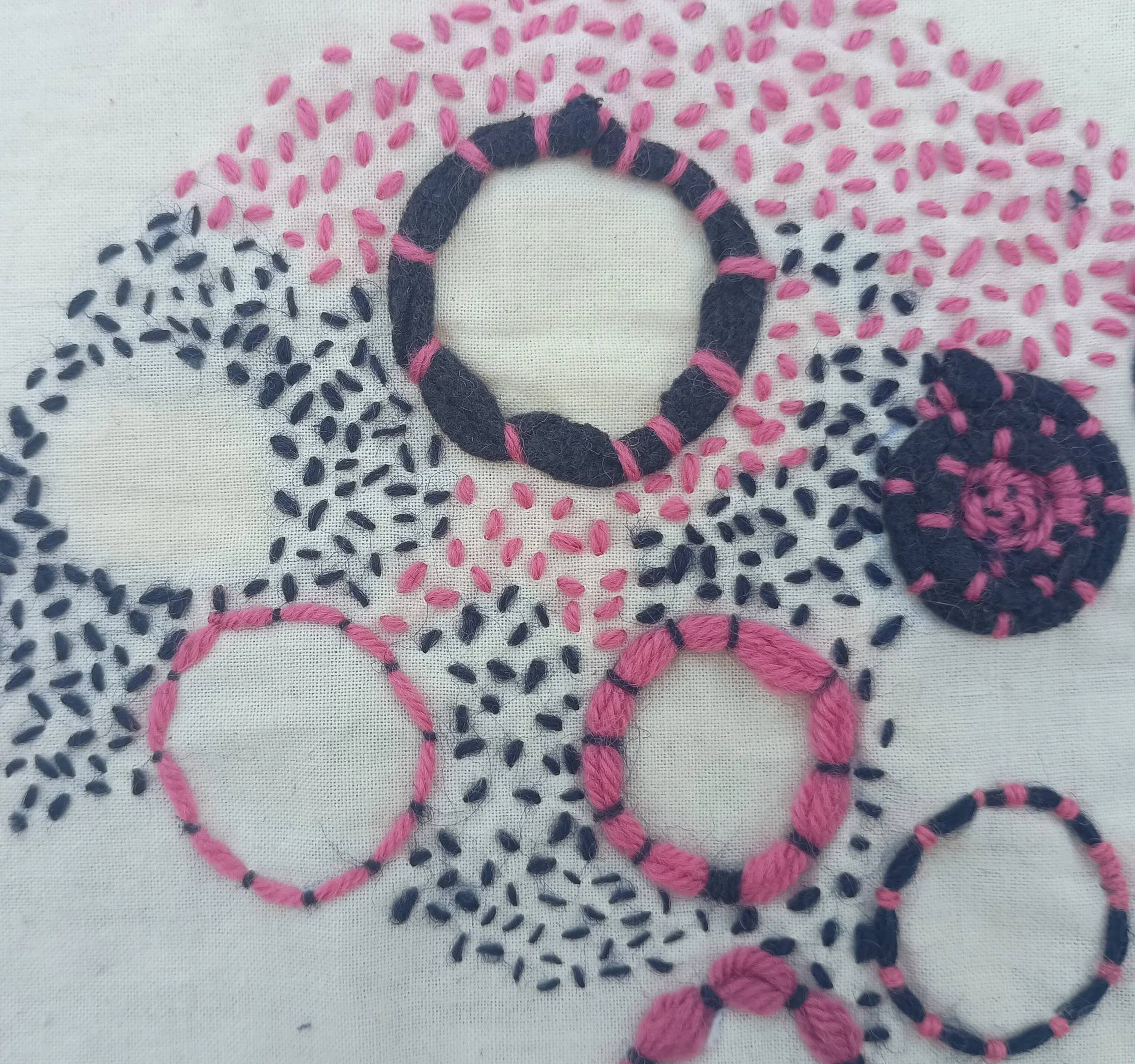 Close-up of embroidery on fabric with black and pink threads forming a ring and other stitched patterns.