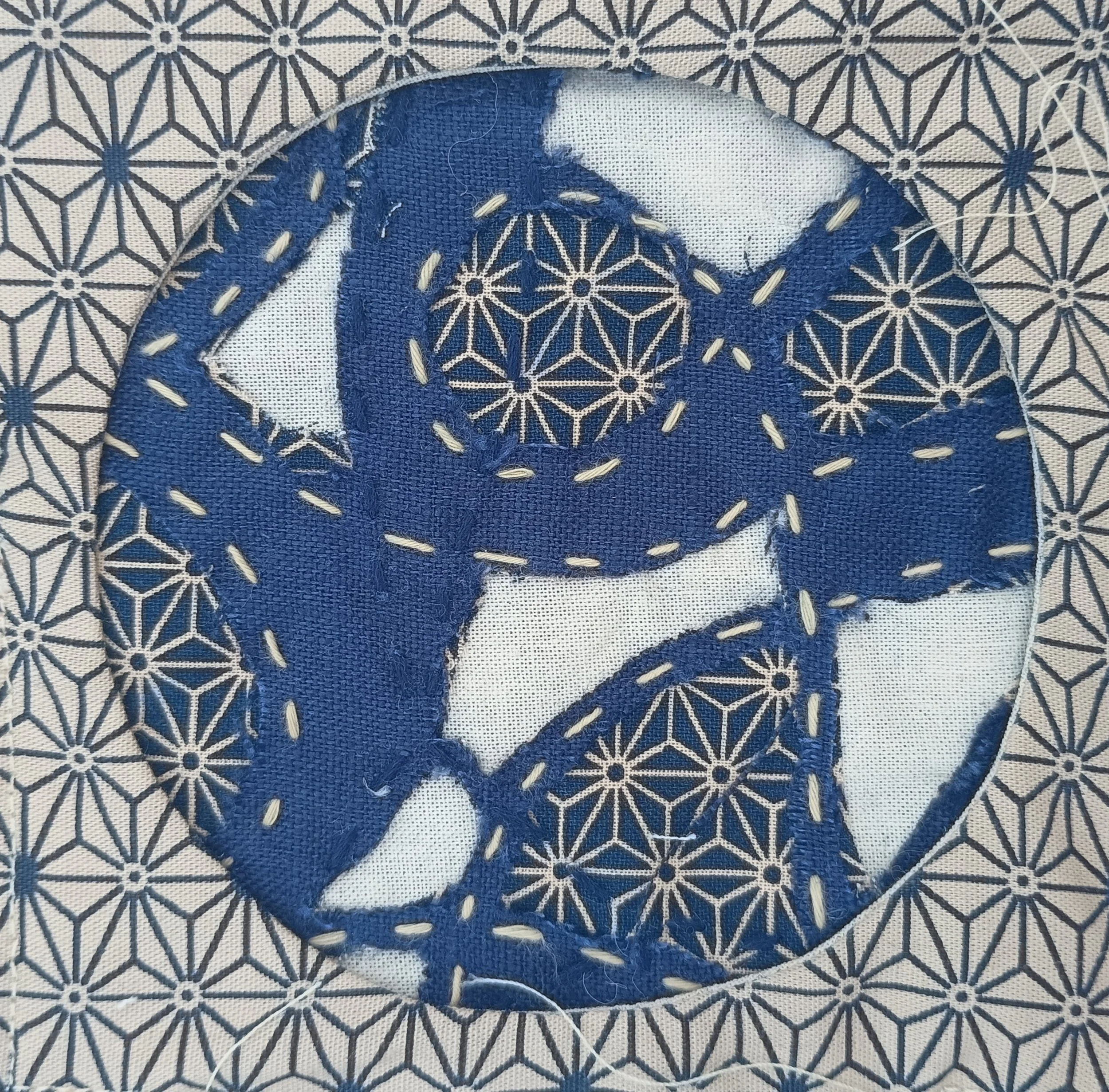 Close-up of a piece of traditional Japanese fabric with a geometric pattern in navy blue and white, featuring a layered circular embroidery design.