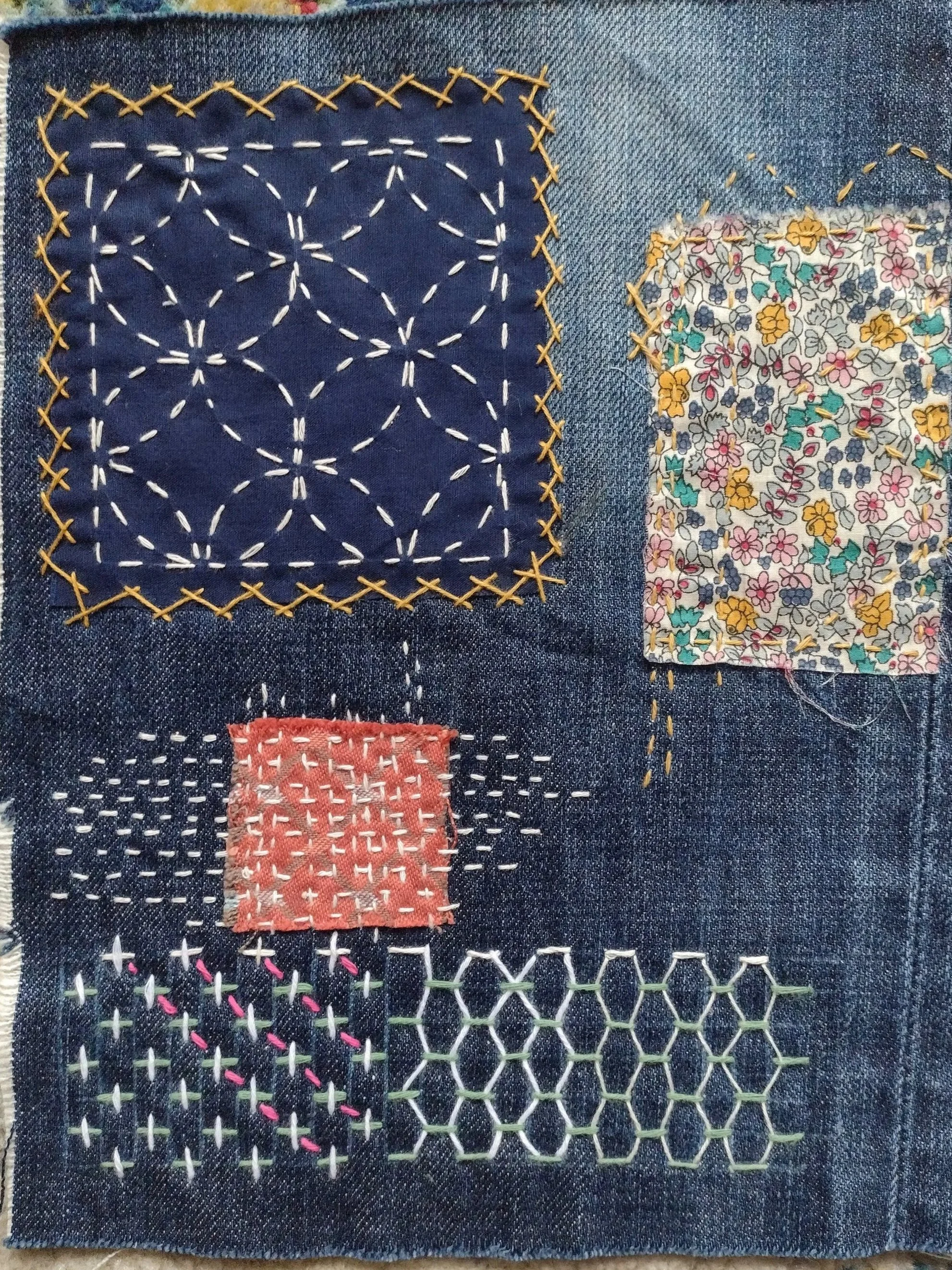 Close-up of denim fabric with embroidered and stitched patches in various shapes and colors.