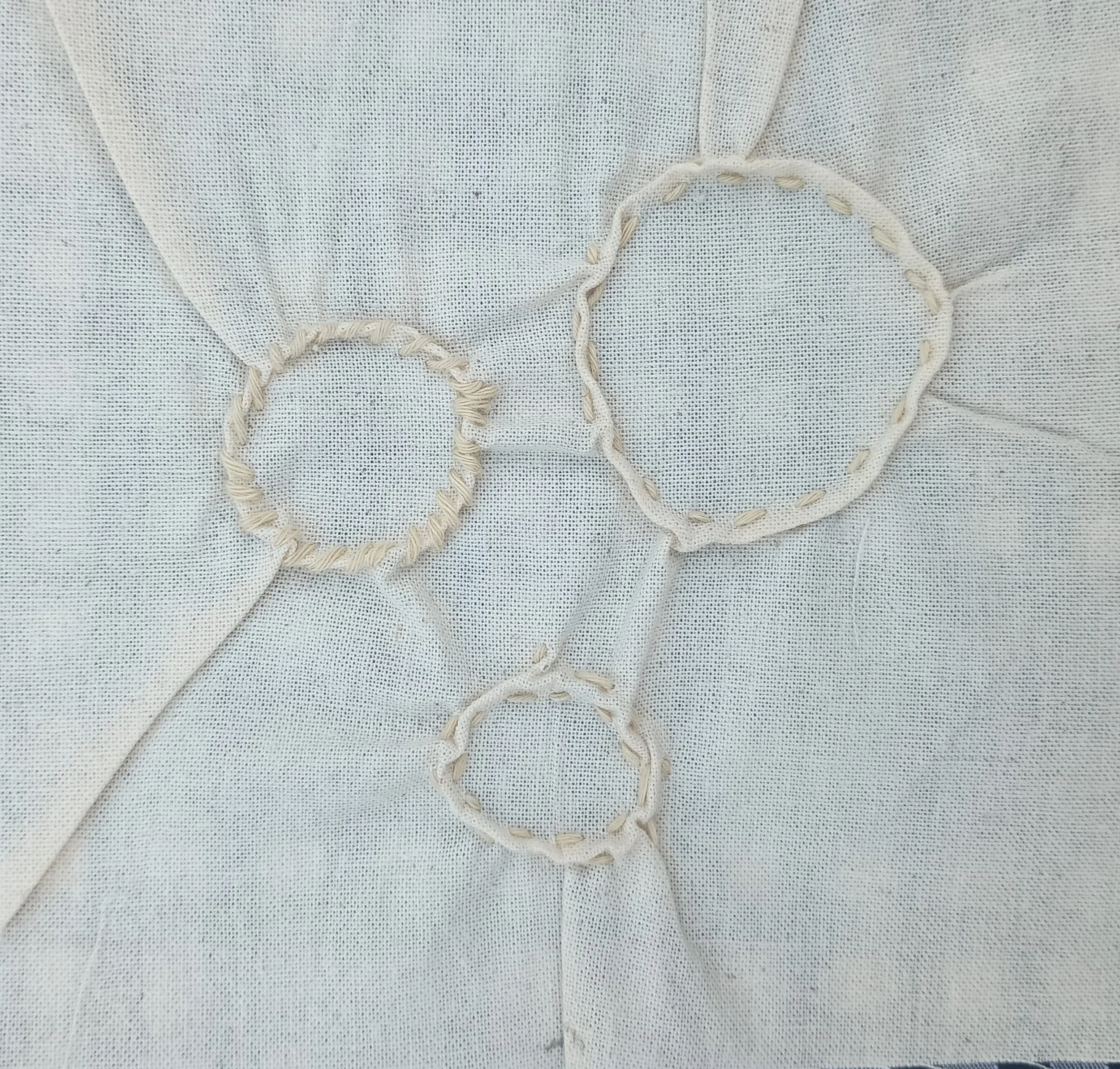 Close-up of light-colored fabric with embroidered heart shapes stitched with thick thread.