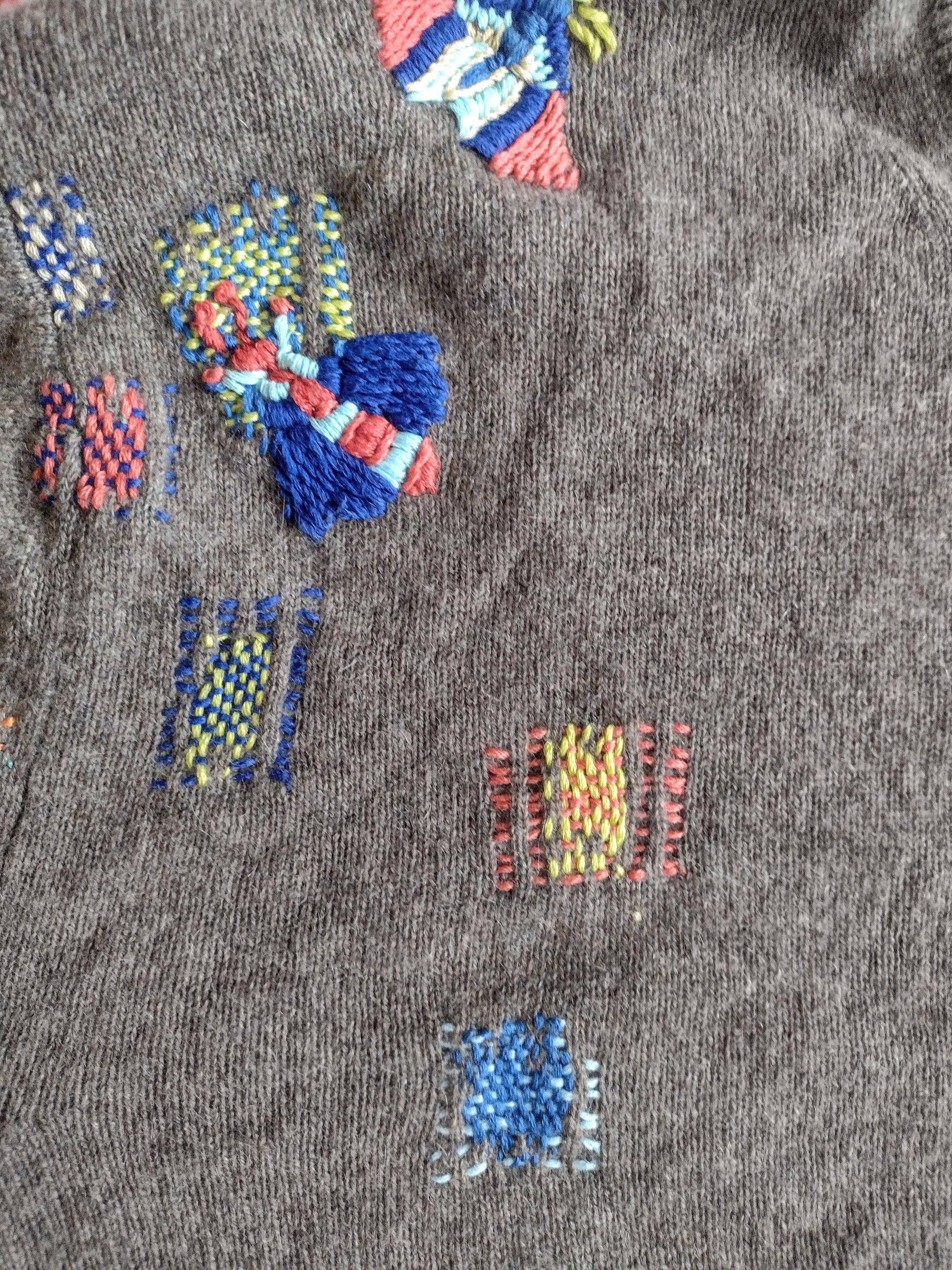 Close-up of embroidered designs on brown fabric featuring colorful flowers and leaves, created with various stitches and thread colors.