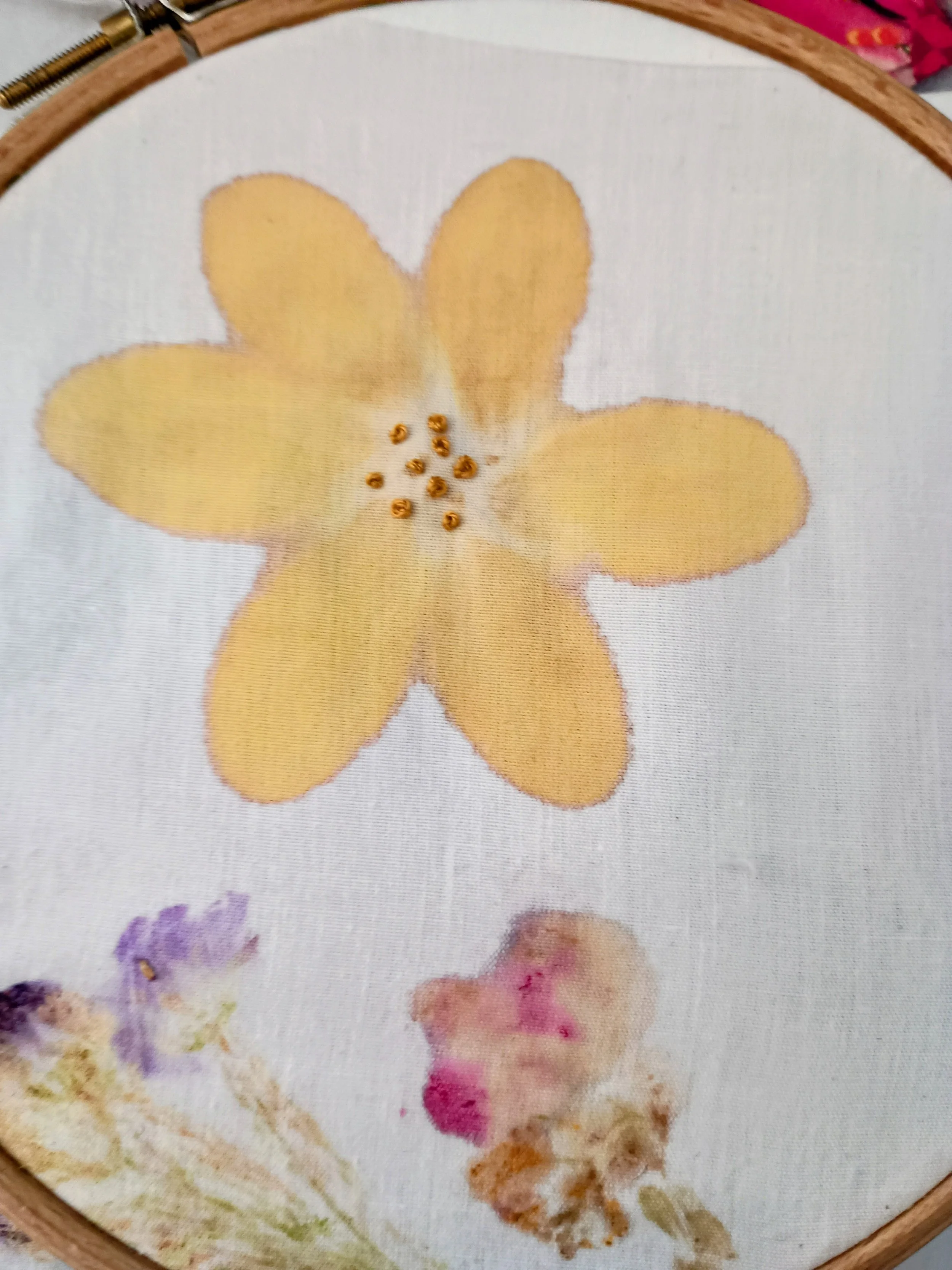 Embroidery hoop with a partially finished yellow flower design on fabric.