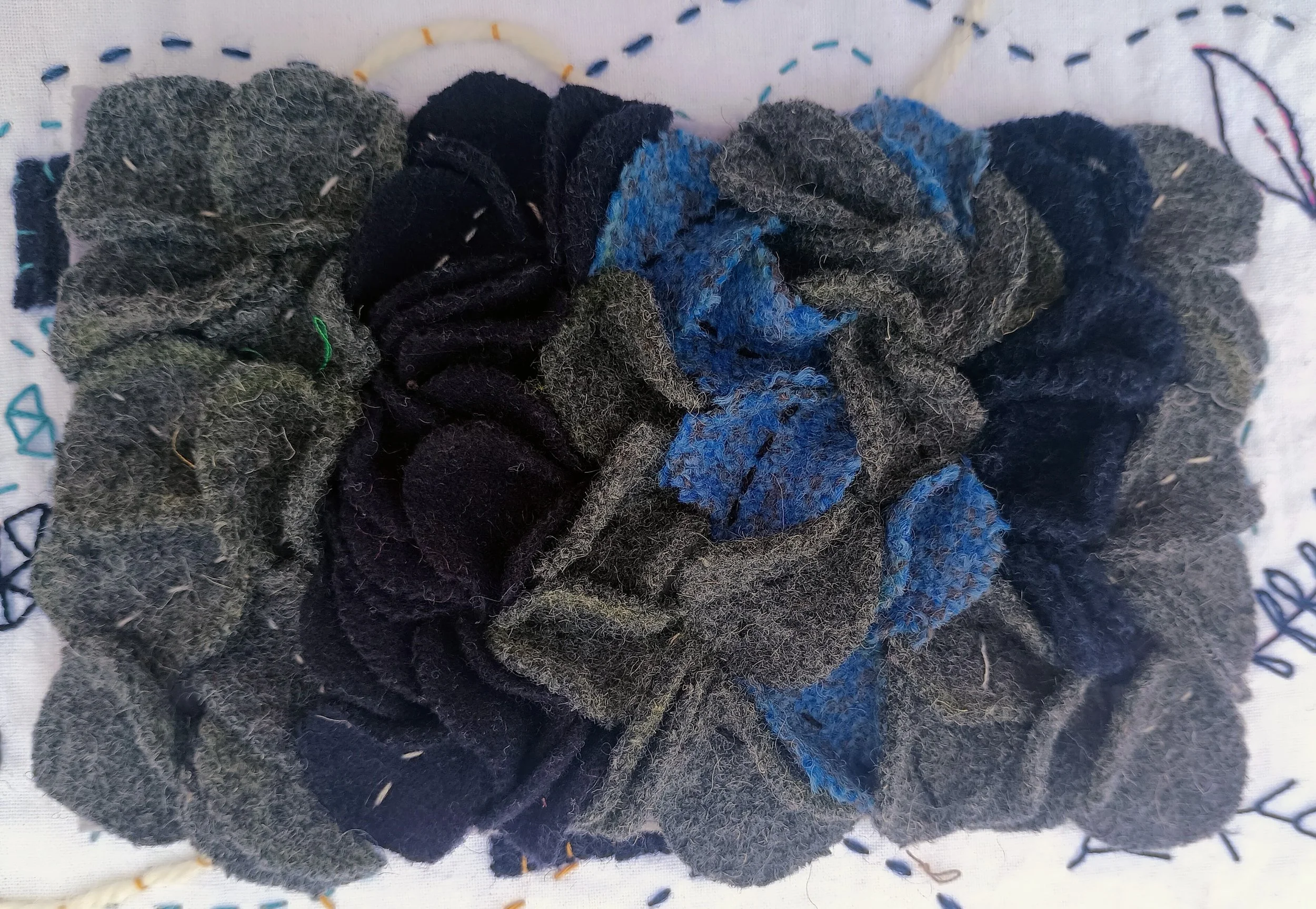 A collection of black, gray, and blue cloth hair ties and scrunchies on an embroidered white fabric background.