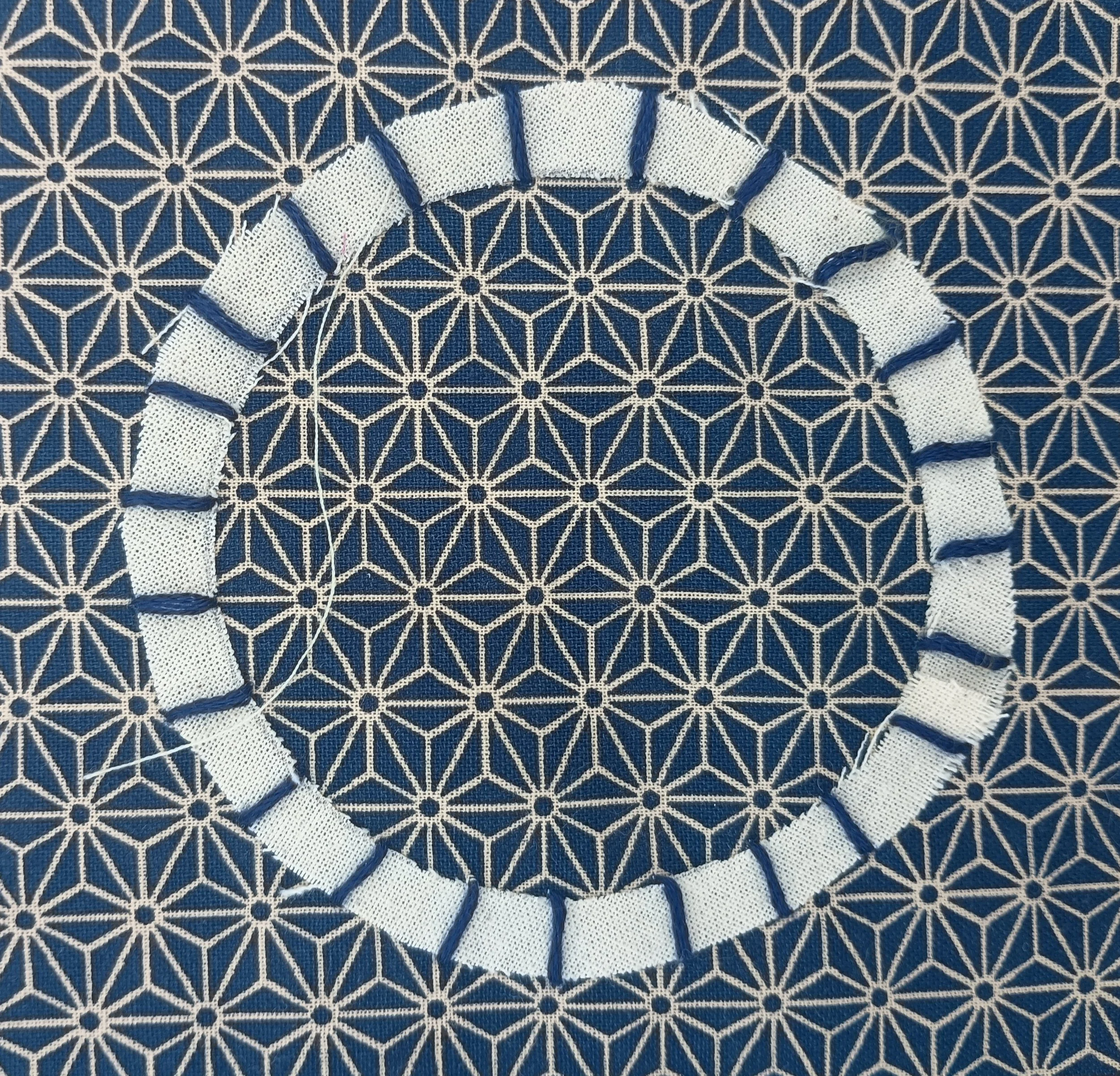 Close-up of a fabric with a white and blue geometric pattern, featuring a section of white mesh with blue embroidery.