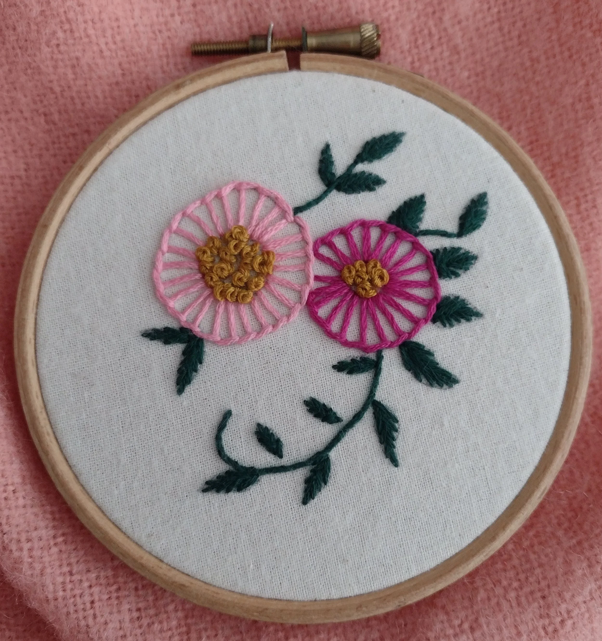 Embroidery hoop with floral embroidery on white fabric, featuring pink and yellow flowers with green leaves.