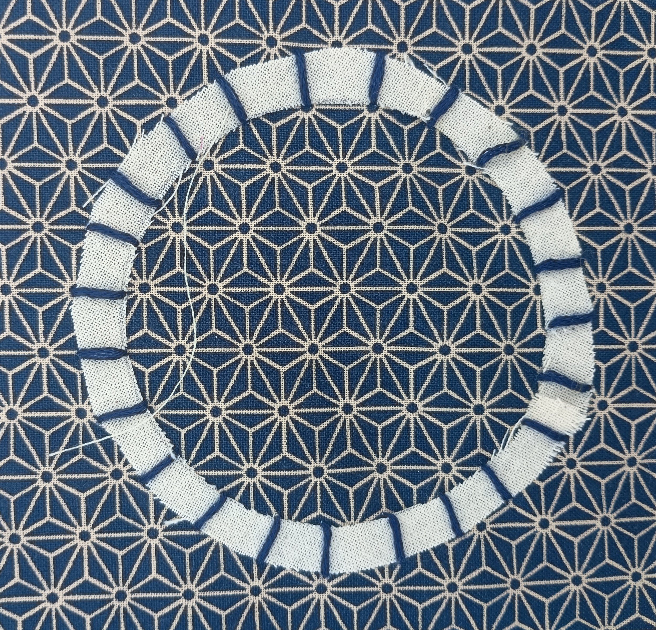 Close-up of a woven fabric with a white geometric pattern on a blue background, featuring a section with frayed and torn white threads.