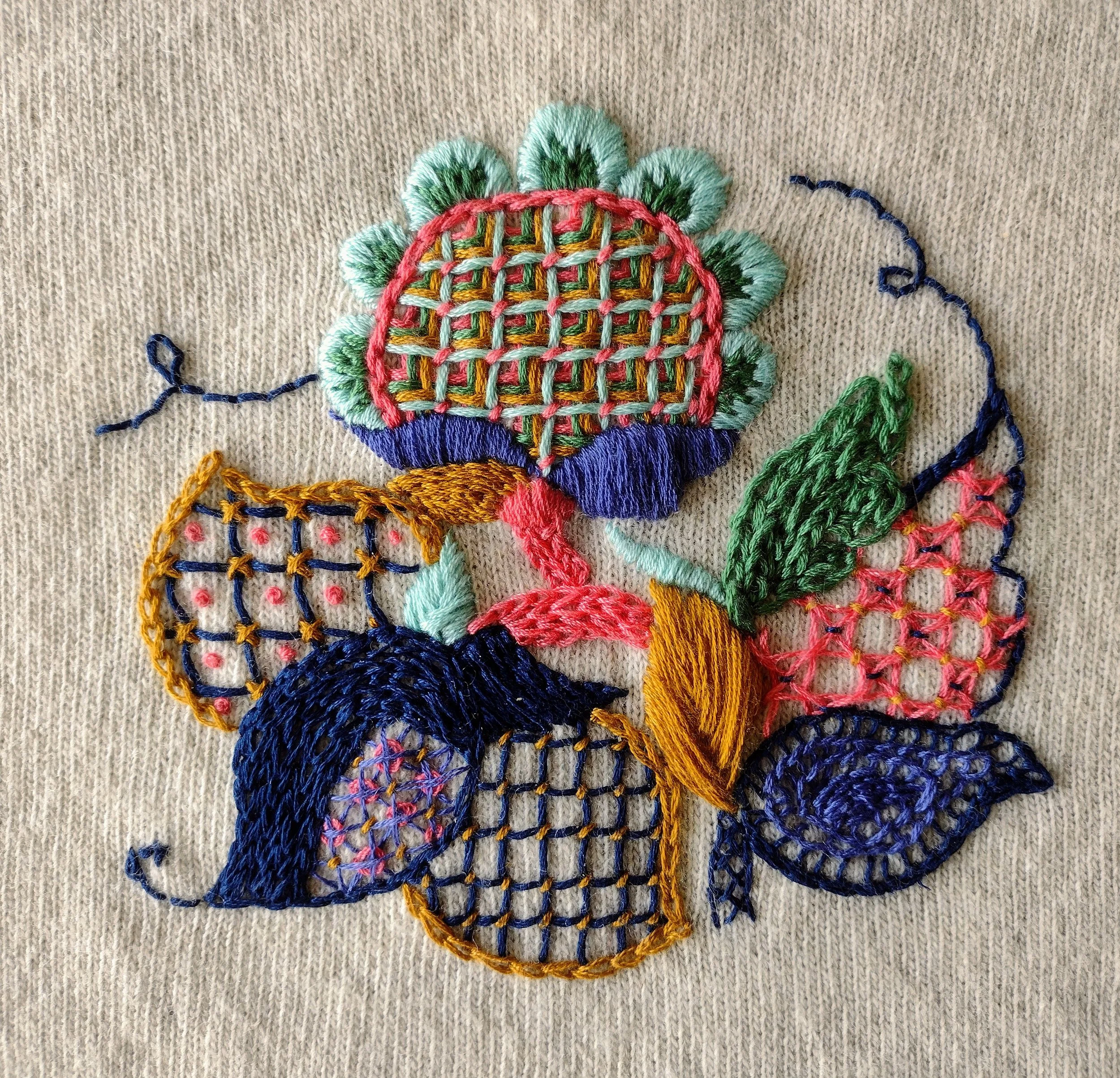 Close-up of colorful embroidered flower on beige fabric background.