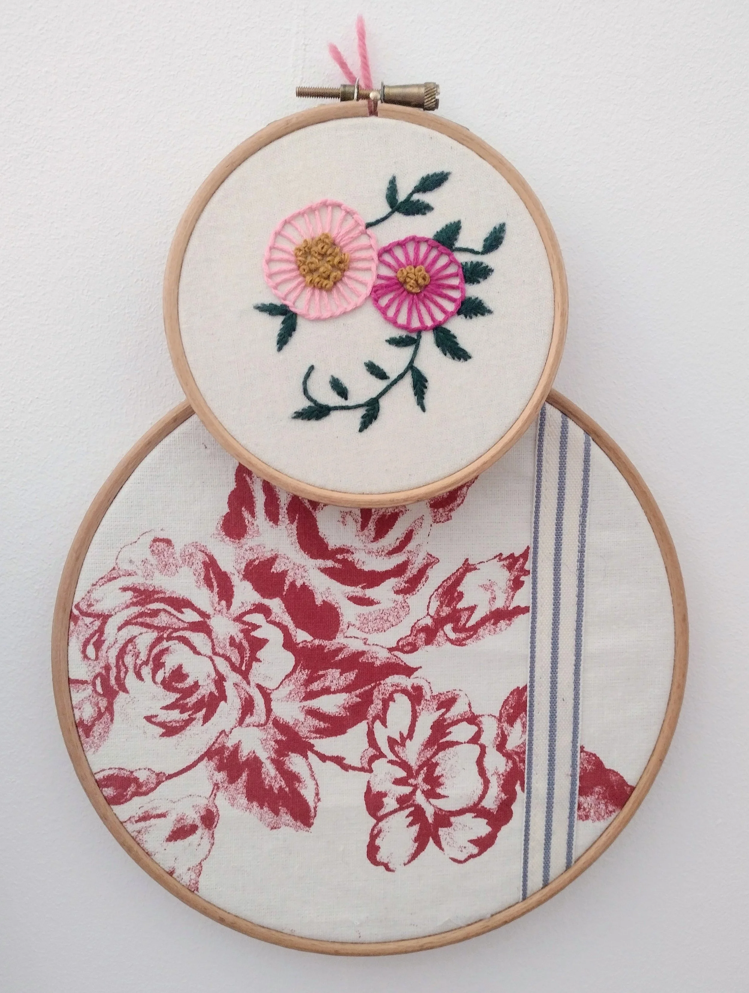 Embroidery hoop with pink stitched flowers and green leaves on white fabric.