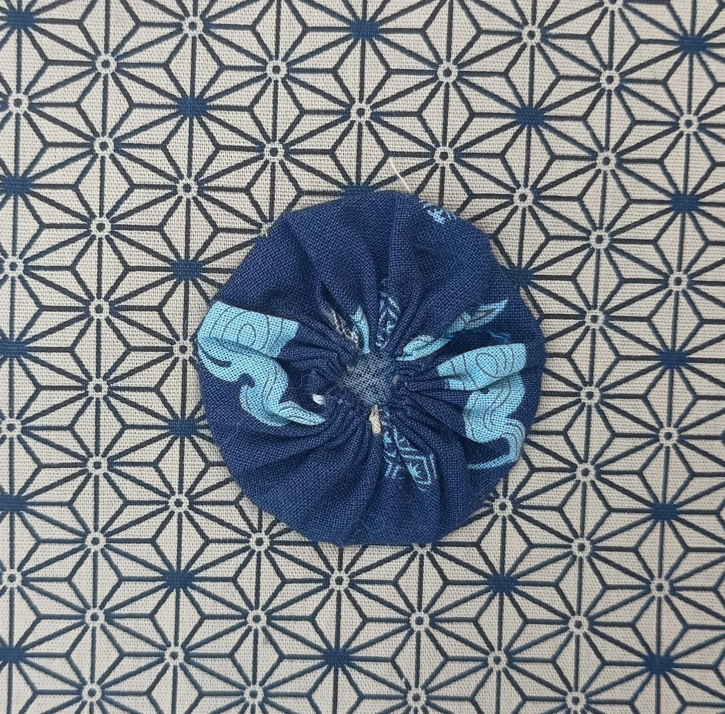 The photo shows the feet of a person wearing dark blue jeans and a pair of black slip-on shoes with white soles, standing on a patterned tile floor. The floor tiles feature a repeating geometric design with black, white, and dark blue colors.
