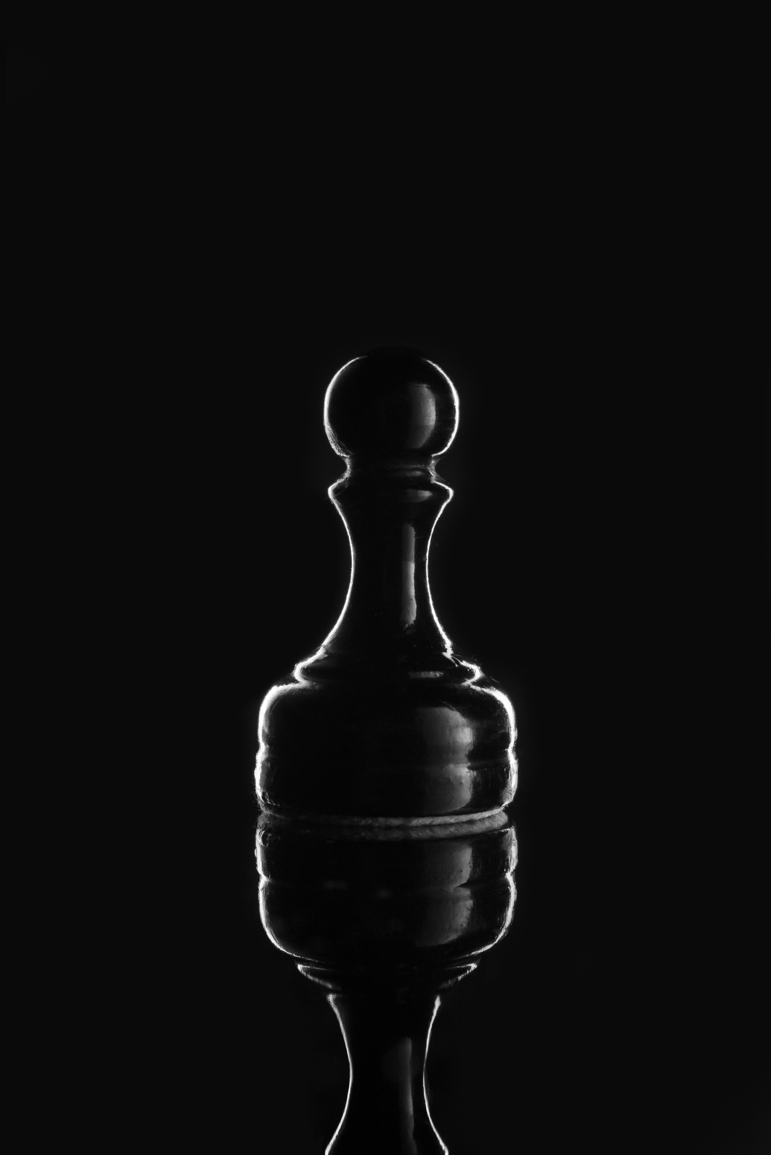 Silhouette of a pawn chess piece with a reflective surface, illuminated from the sides against a black background.