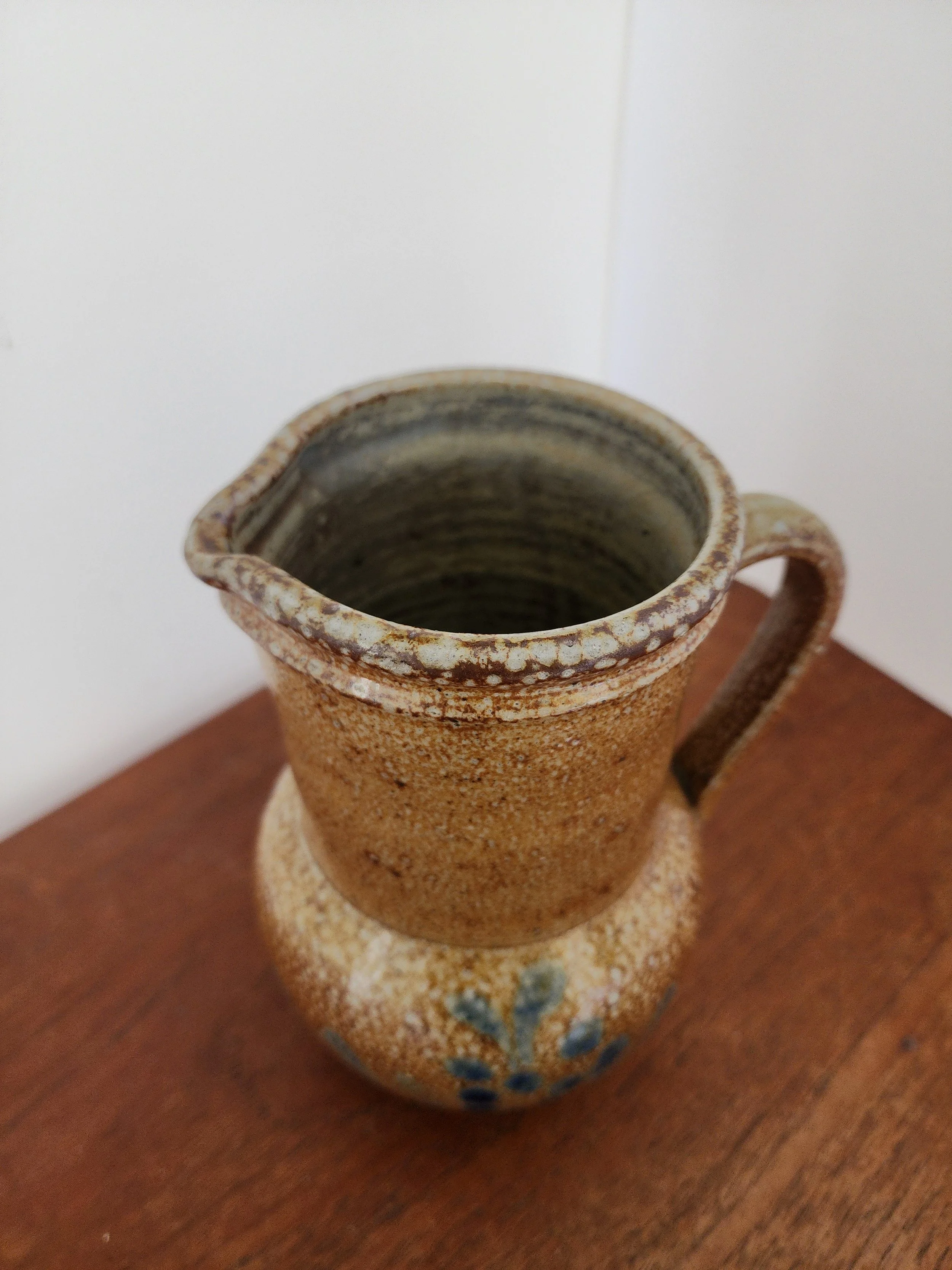 Side view of brown glazed ceramic pitcher showing handle and speckled texture.”