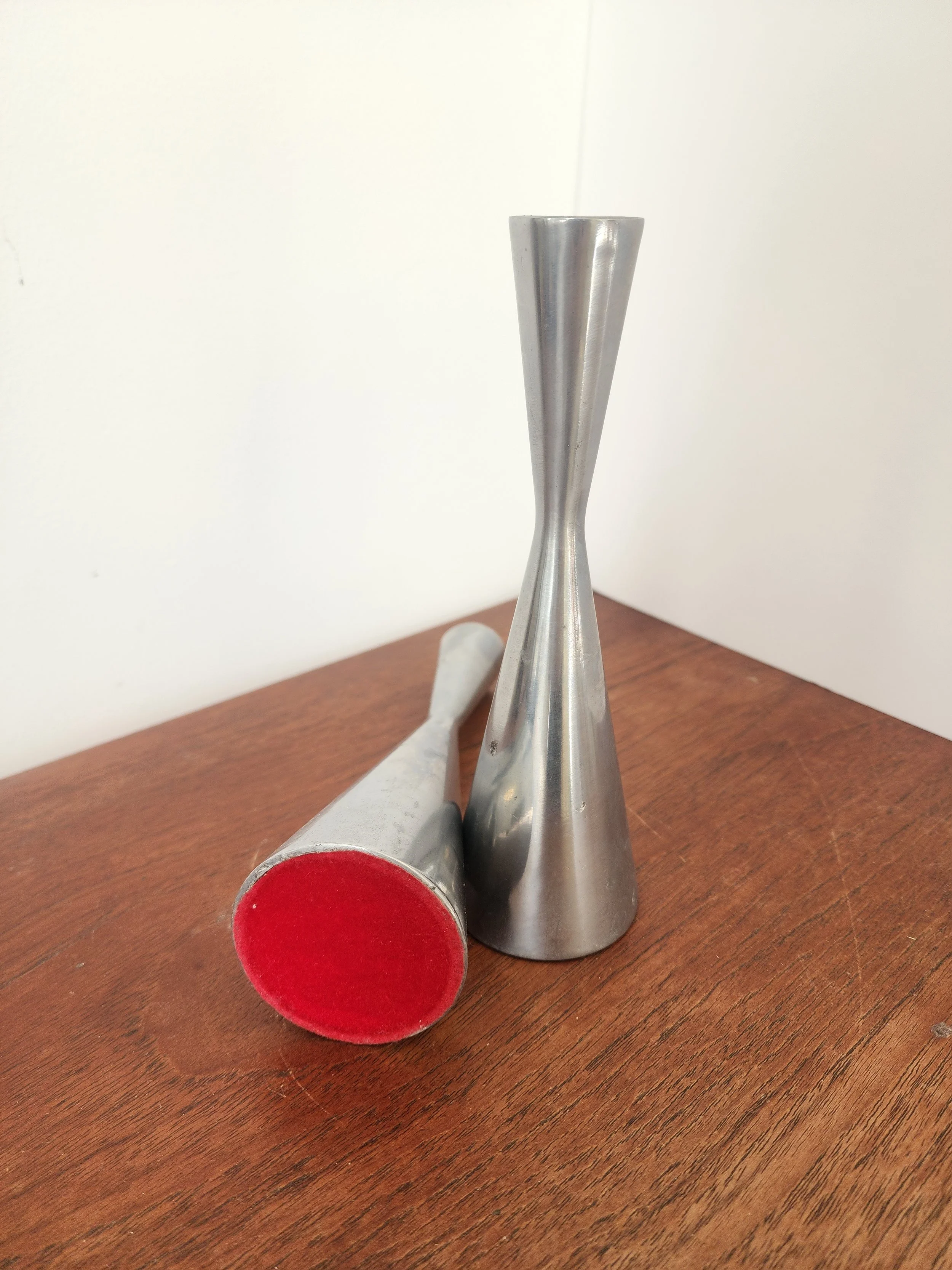 “Modernist brushed metal candlestick duo holding twisted burgundy taper candles.”