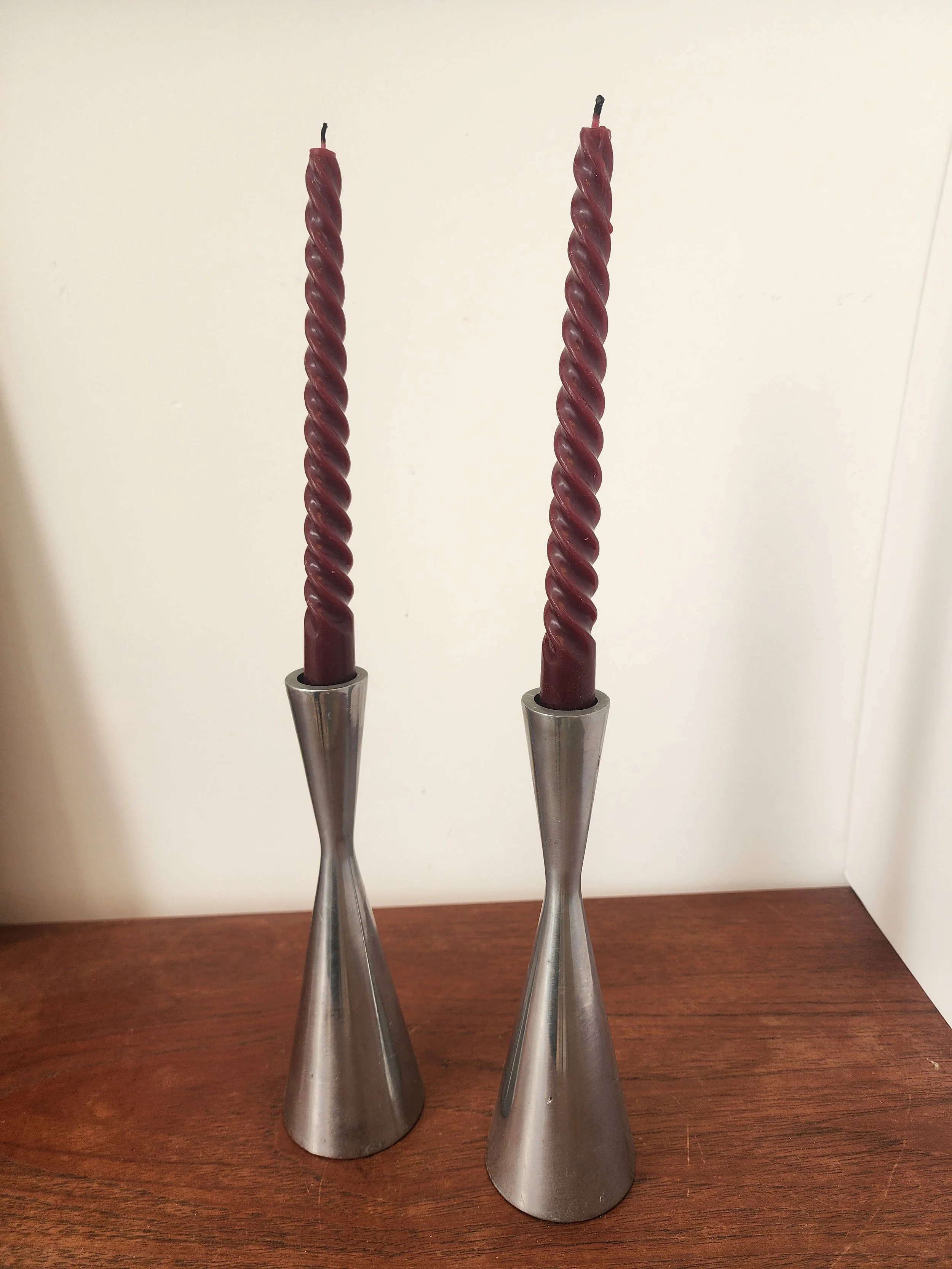 “Vintage hourglass-shaped metal taper holders displayed with tall burgundy candles.”