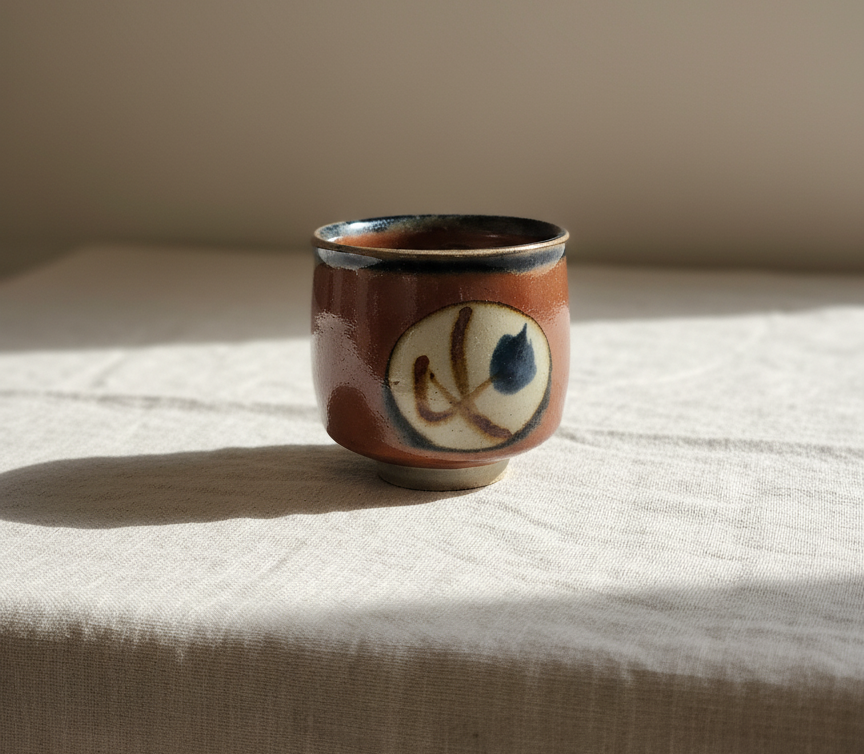 Vintage Japanese pottery cup with hand-painted brush design on linen cloth.