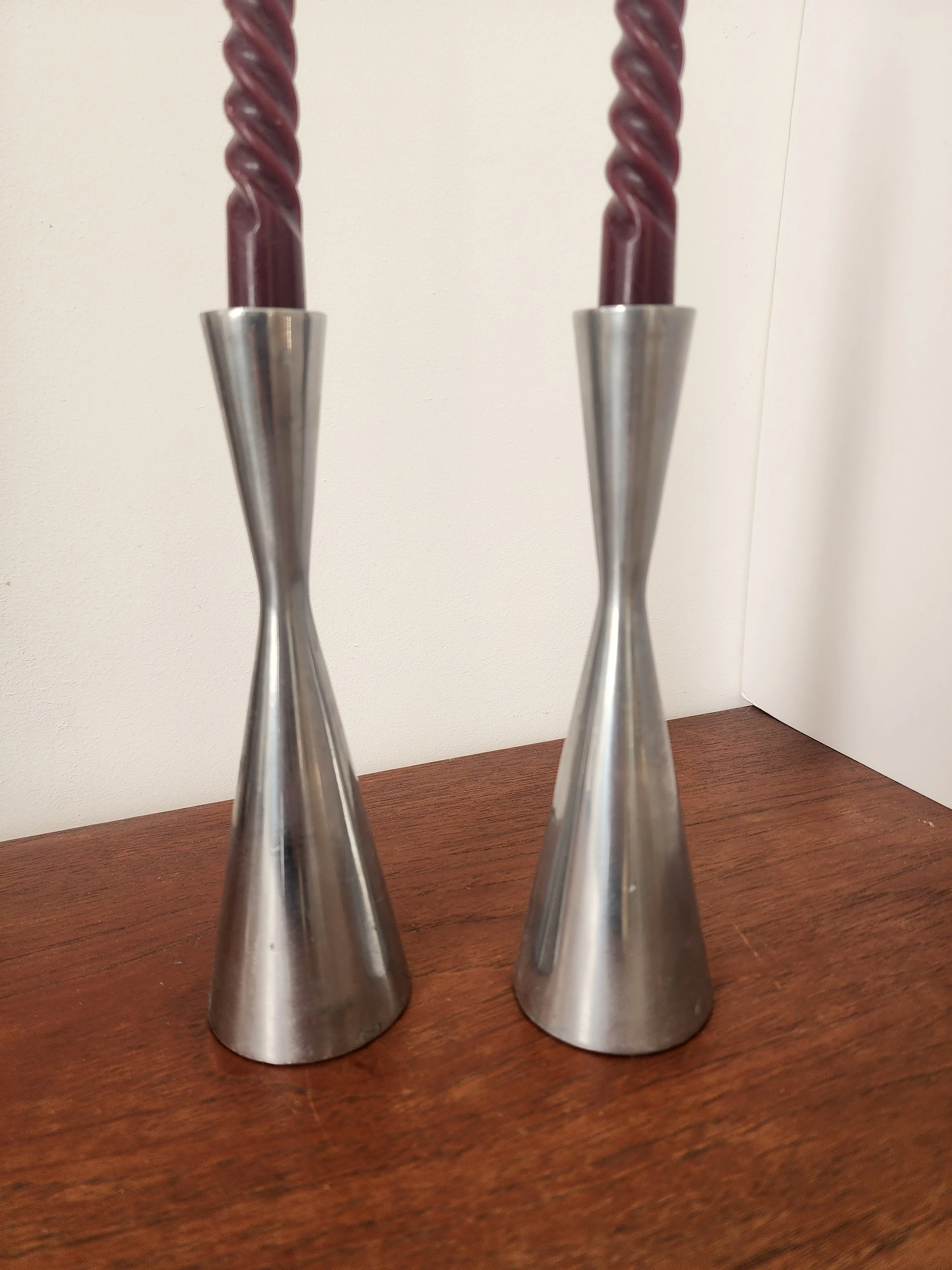“Pair of silver modernist metal candle holders with burgundy spiral candles on a linen cloth.”