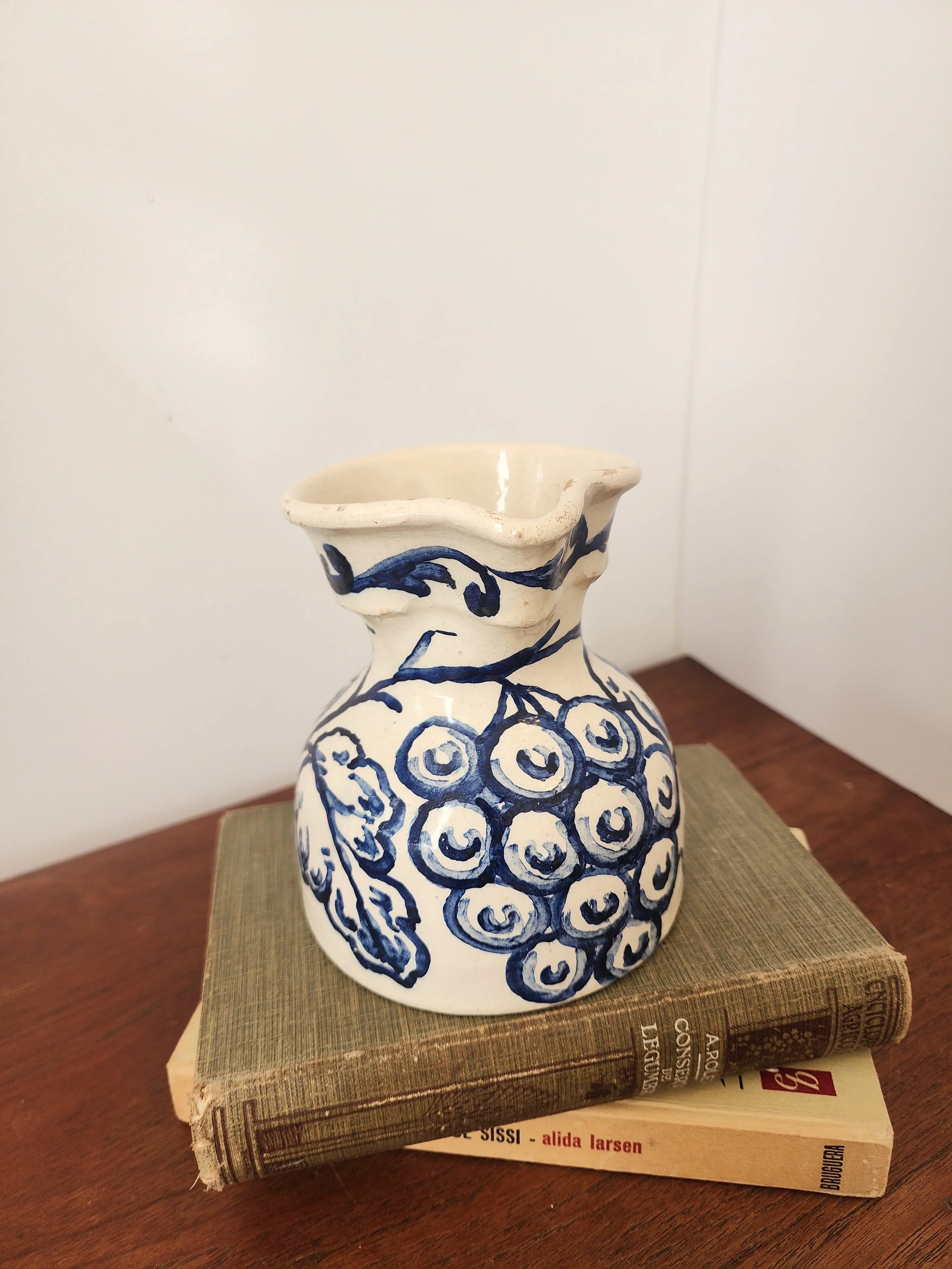 “Rustic hand-painted ceramic jug in blue and white displayed against a beige wall.”