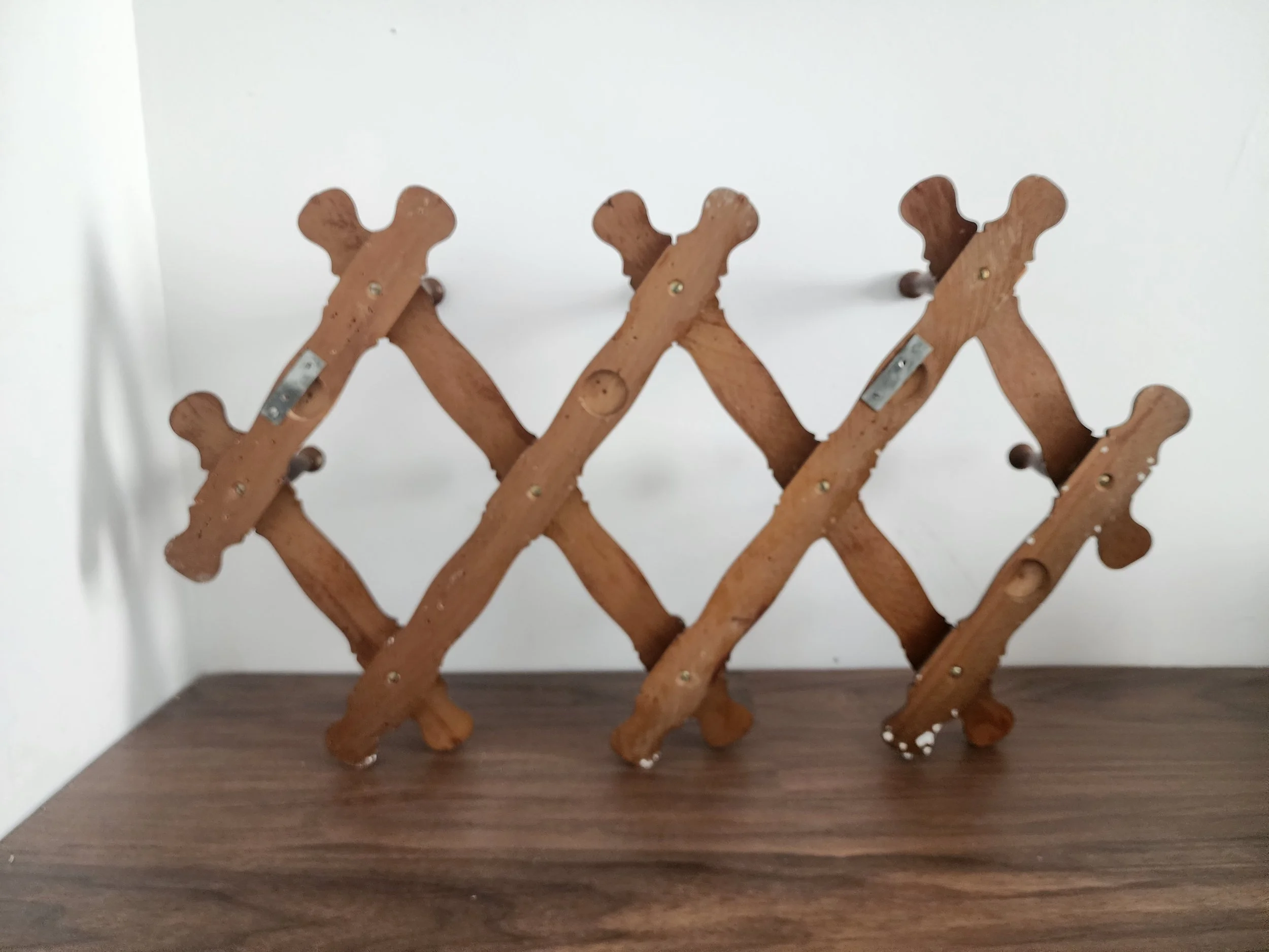 Vintage expandable wooden coat rack fully extended on wall.