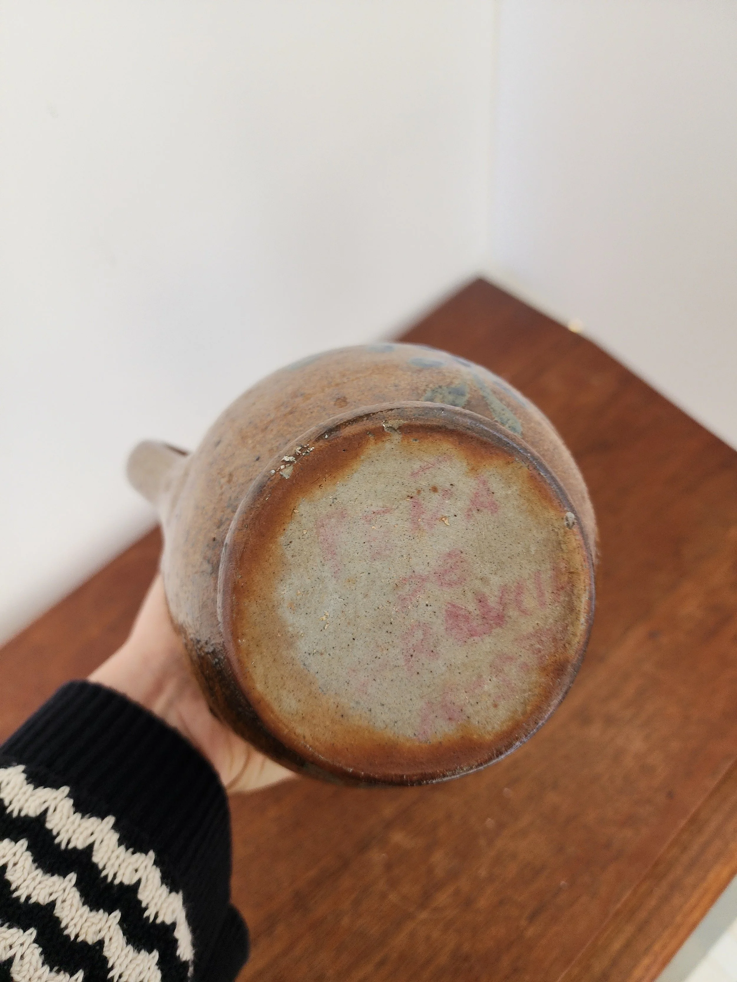 Base detail of handmade stoneware jug with textured glaze and folk-inspired design.”