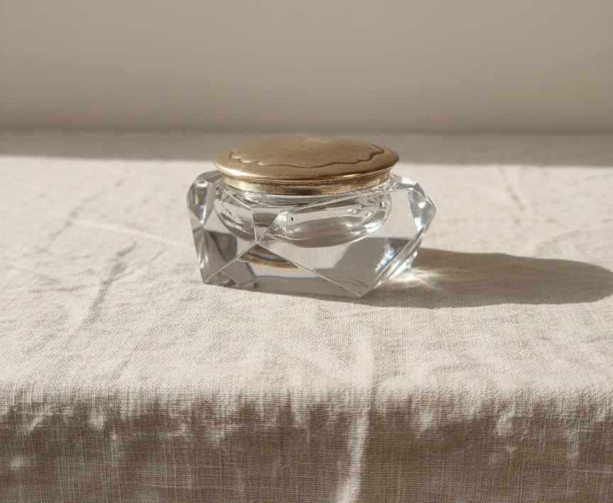 Vintage cut glass vanity jar with silver-plated lid on neutral fabric, faceted sides.