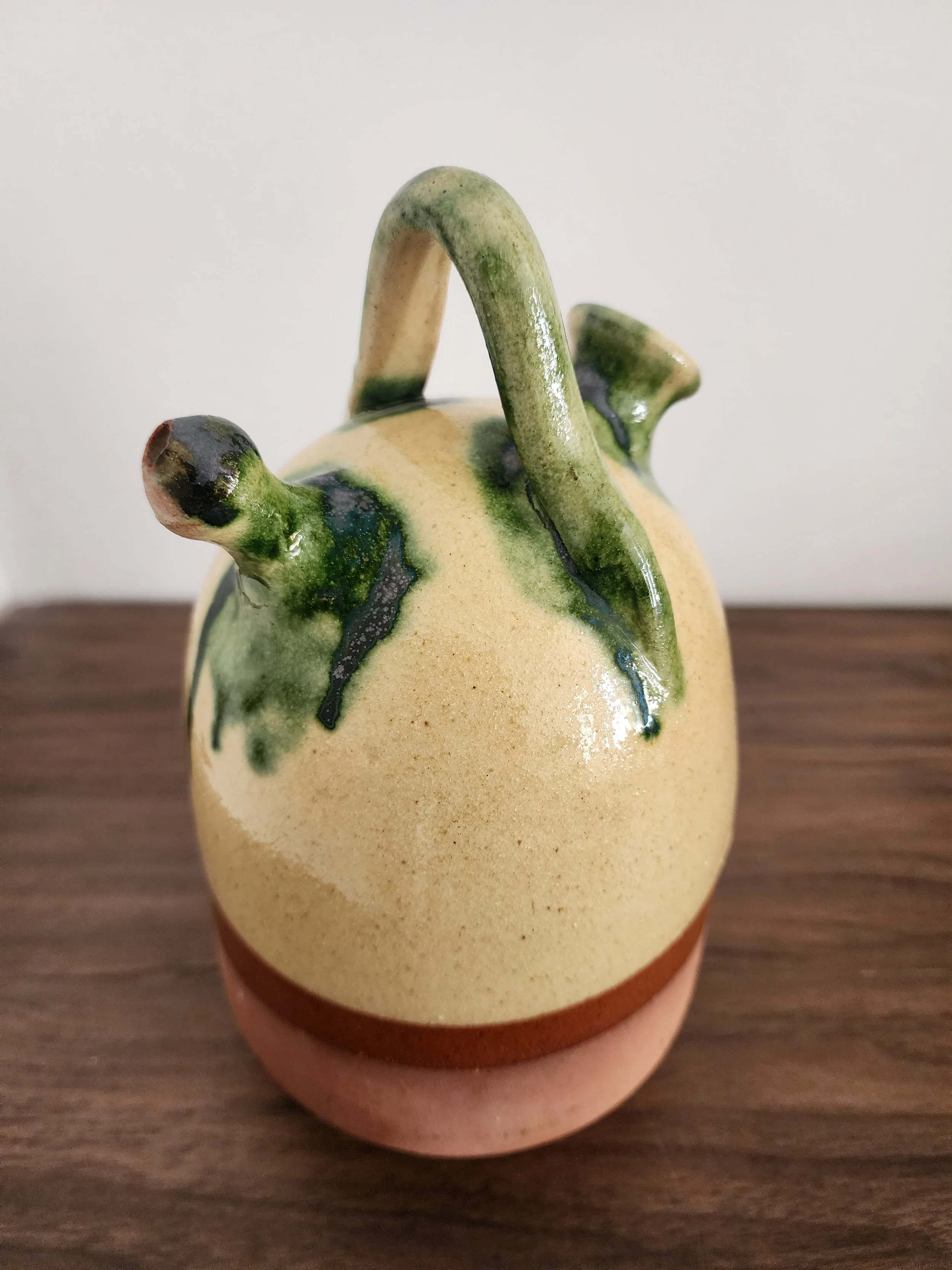 Close-up of green glaze dripping over cream and clay surface.