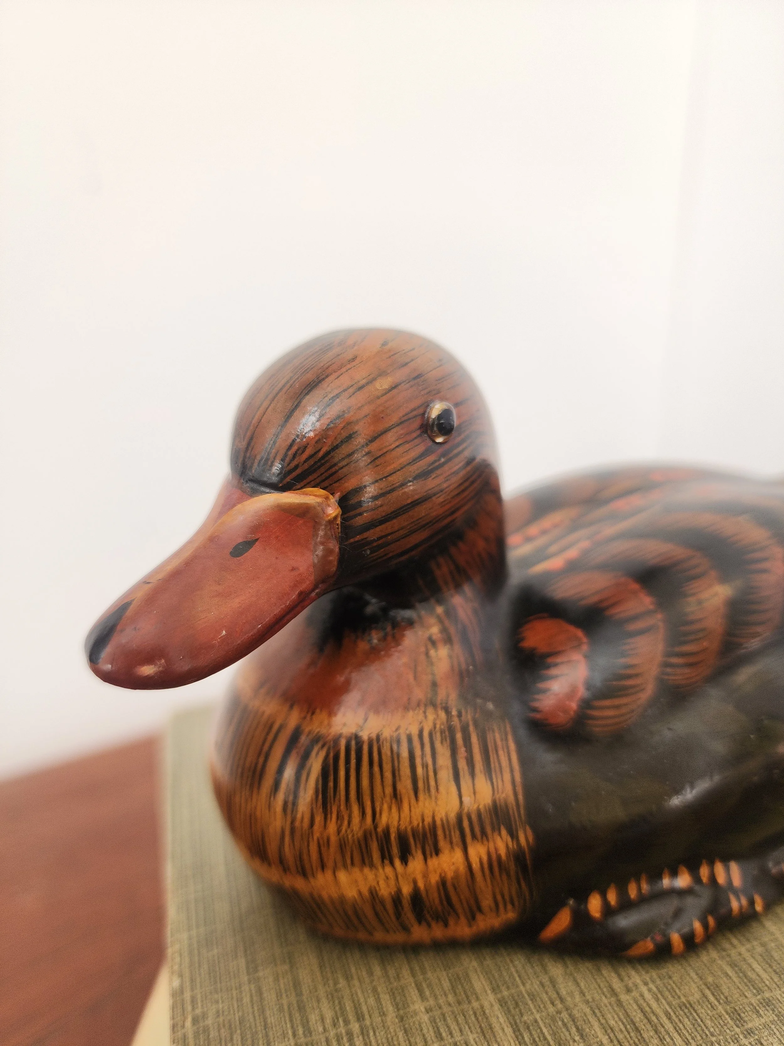 “Small vintage ceramic duck with brown and black detailing on a light fabric surface.”