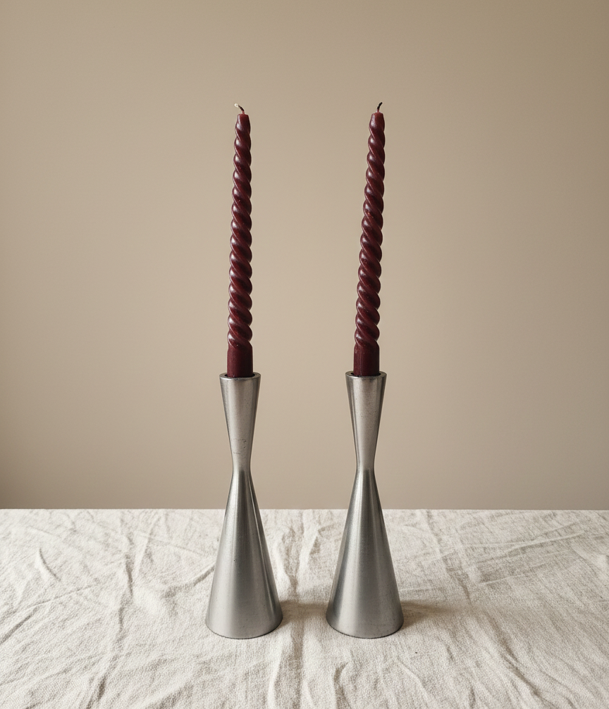 “Pair of silver modernist metal candle holders with burgundy spiral candles on a linen cloth.”