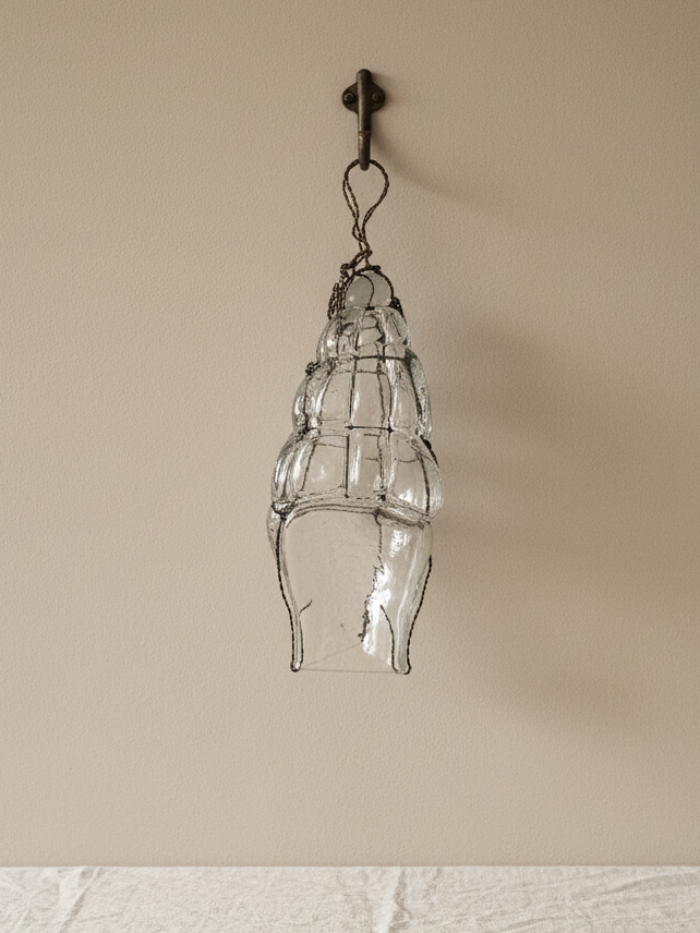 “Vintage hand-blown clear glass sculpture wrapped in aged wire, hanging against a neutral wall.”