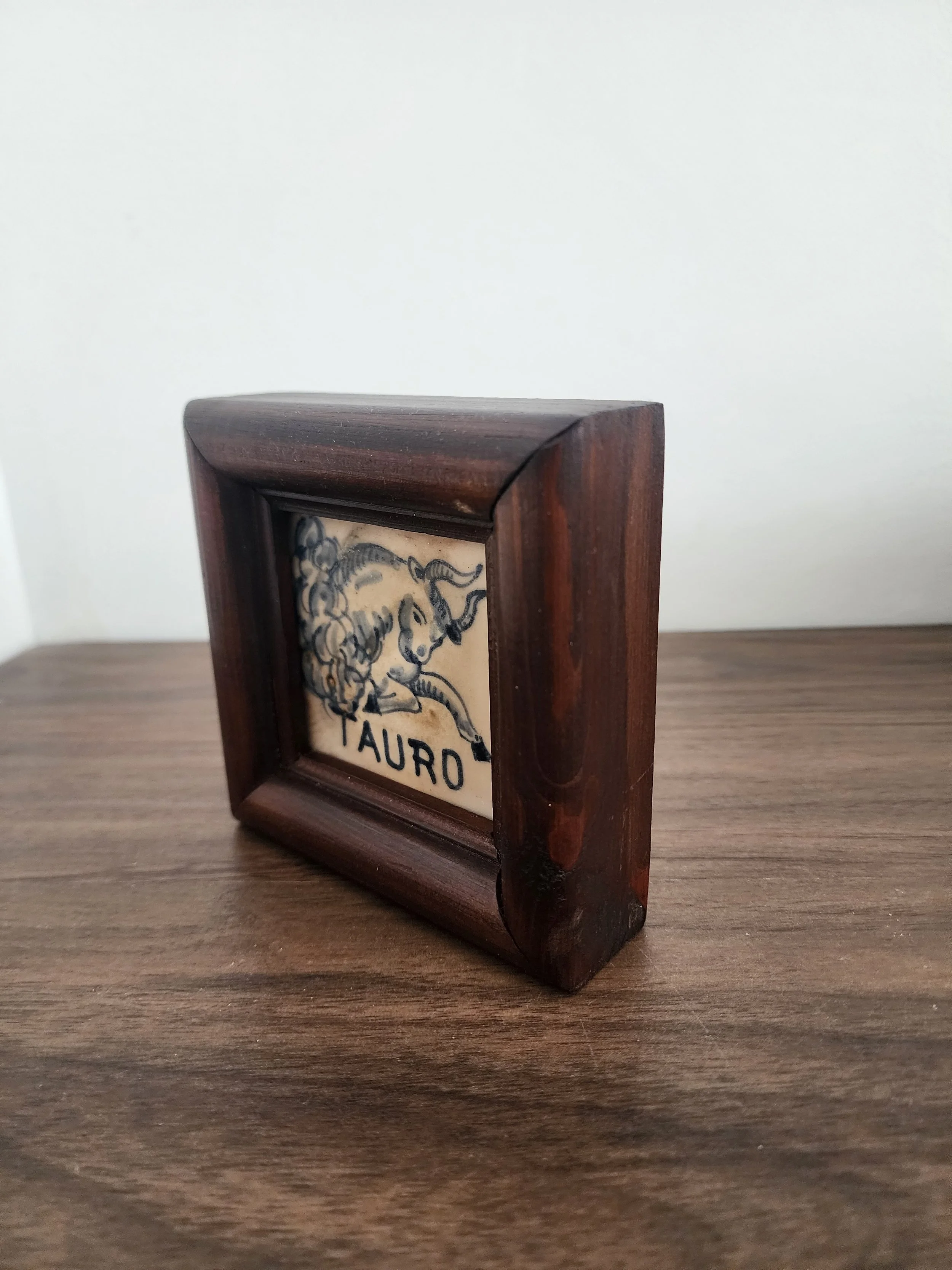 Framed Spanish zodiac tile displayed on beige wall.