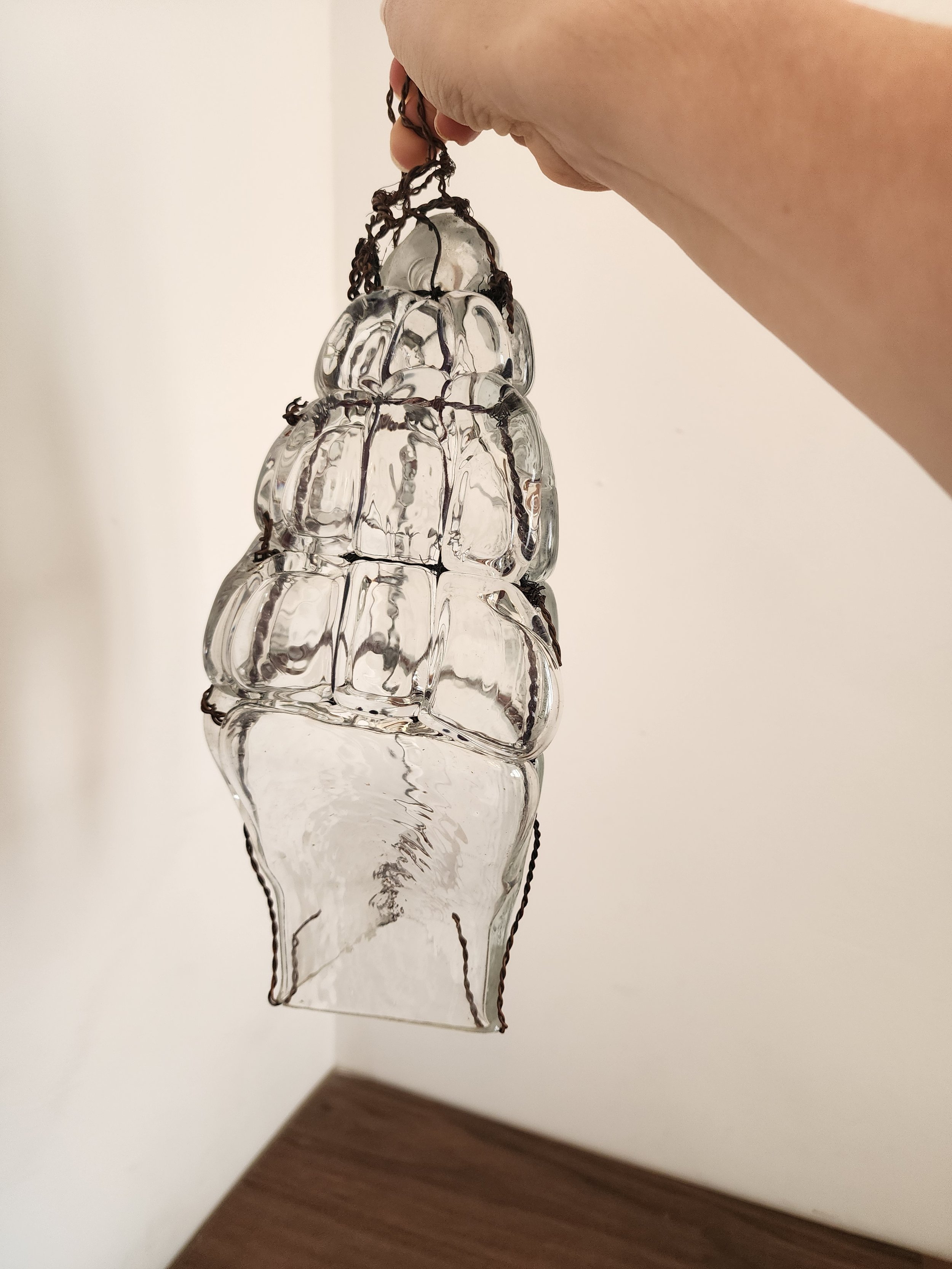 “Clear artisanal glass hanging ornament with sculptural form and rustic wirework design.”