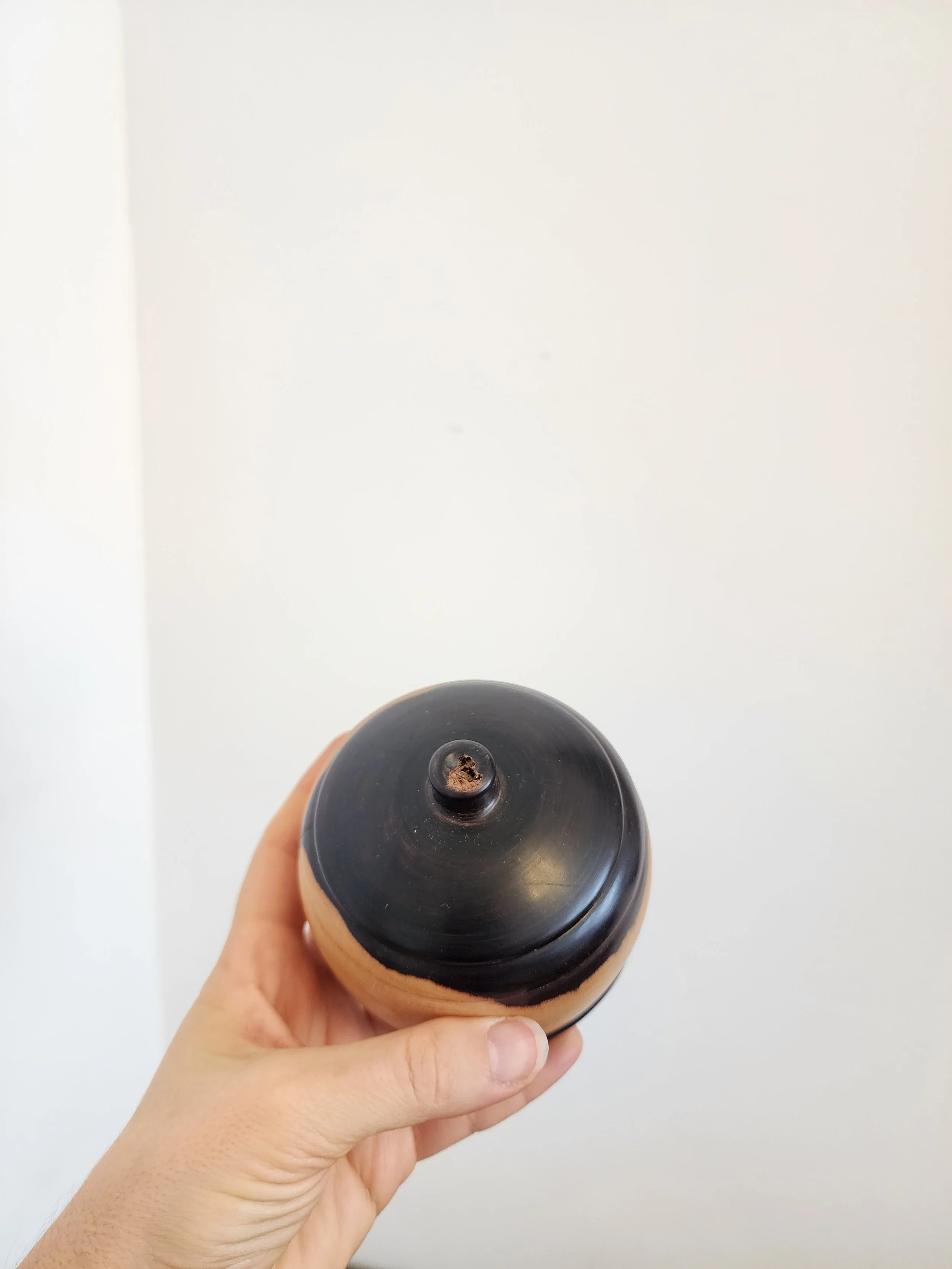Side view of round wooden pot with dark ceramic lid.