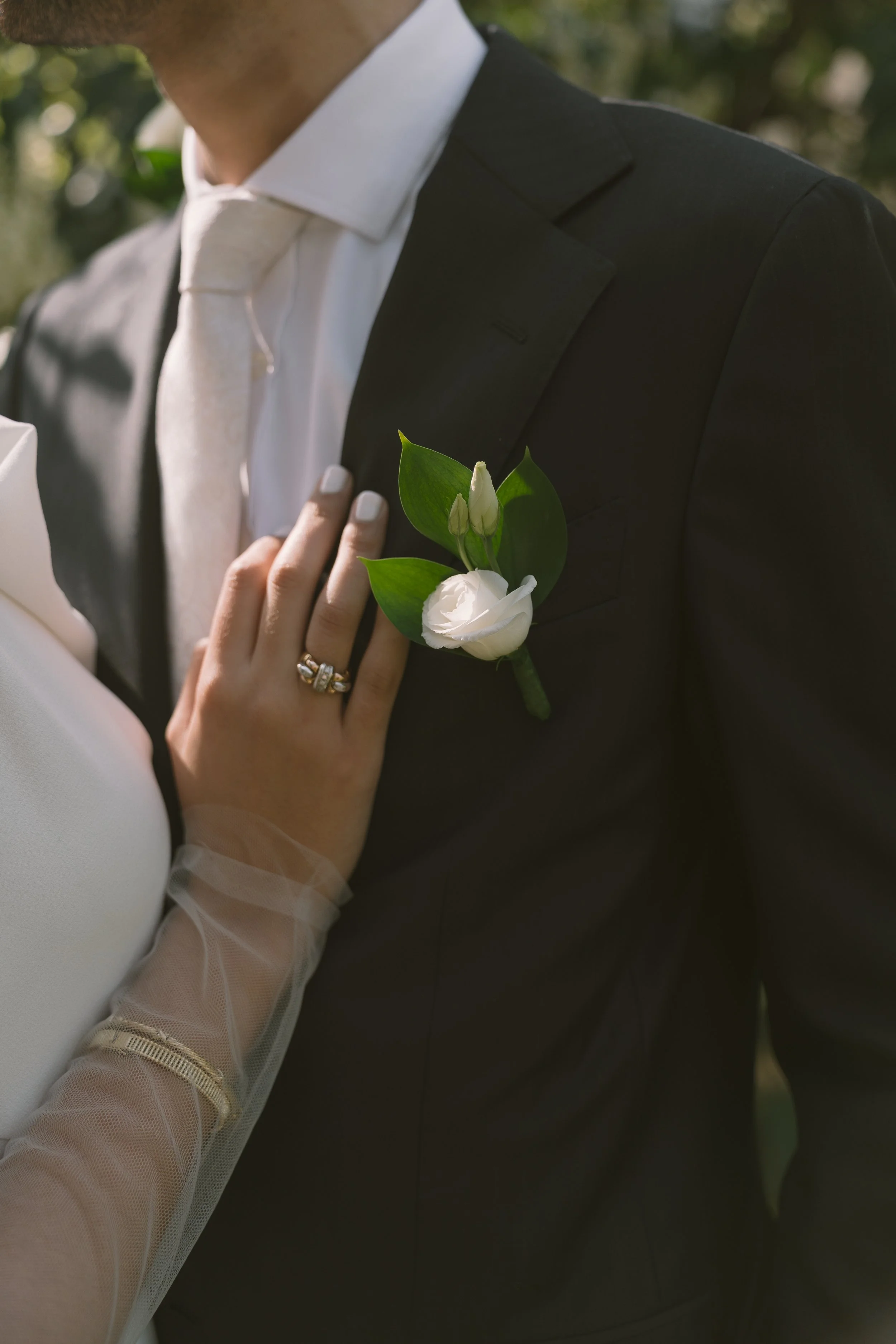Un homme en costume noir avec une boutonnière blanche, une femme en robe blanche avec un gant transparent, lors d'un mariage.