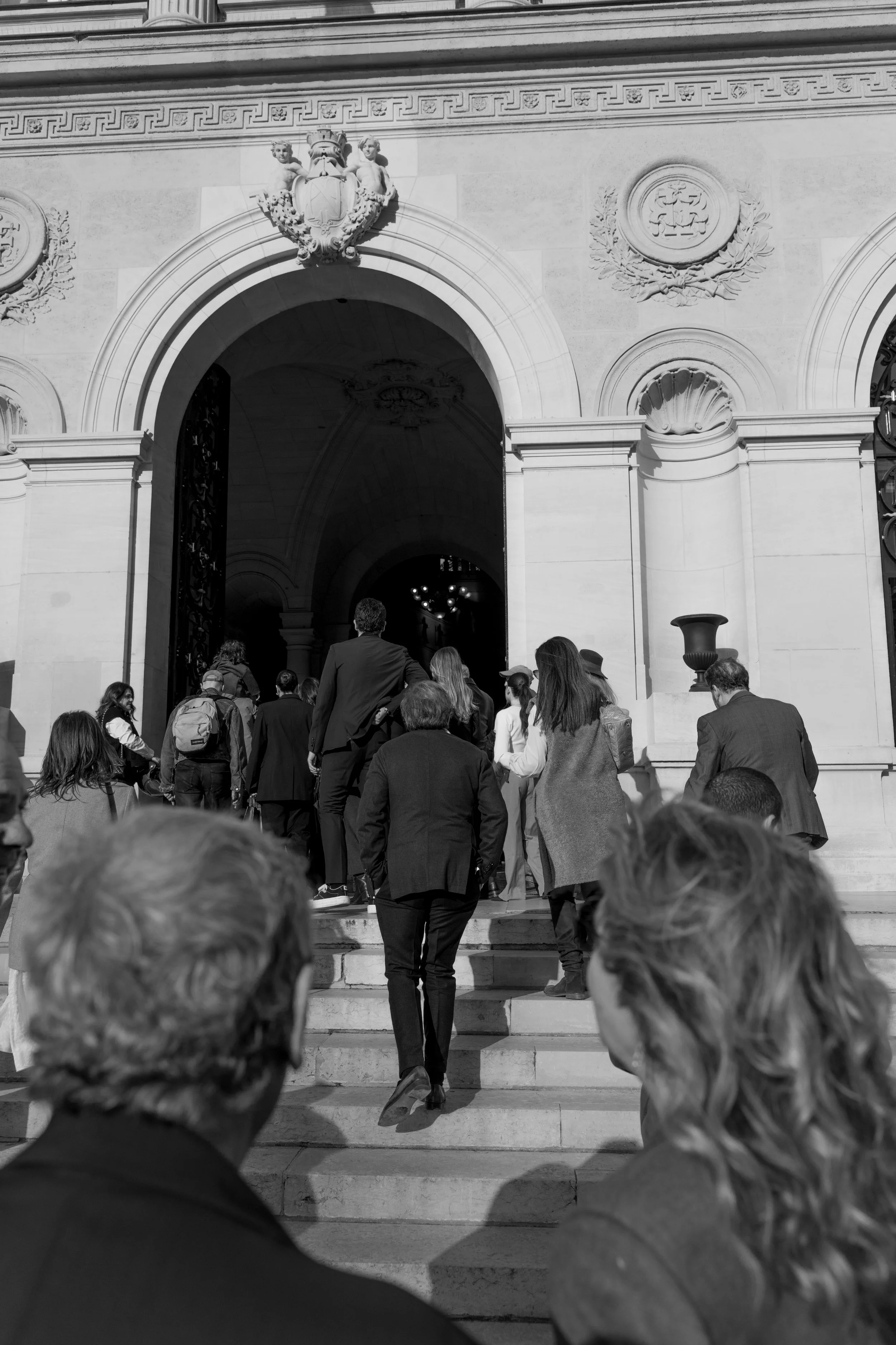 Groupe de personnes montant les escaliers d'un bâtiment historique avec une façade ornée et une porte en arc.