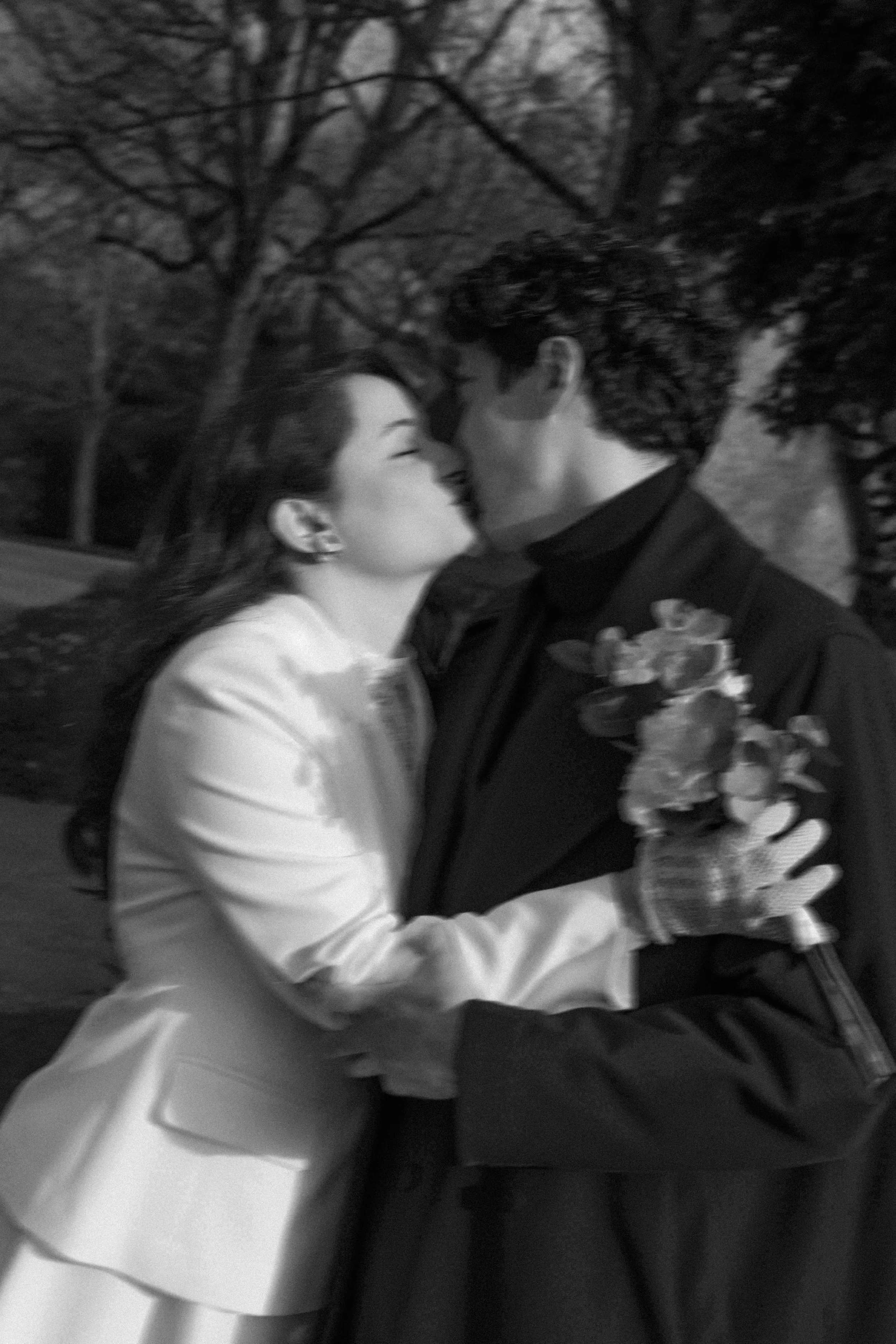Un couple s'embrasse tendrement lors d'une cérémonie ou d'une occasion spéciale en plein air, avec des arbres en arrière-plan.