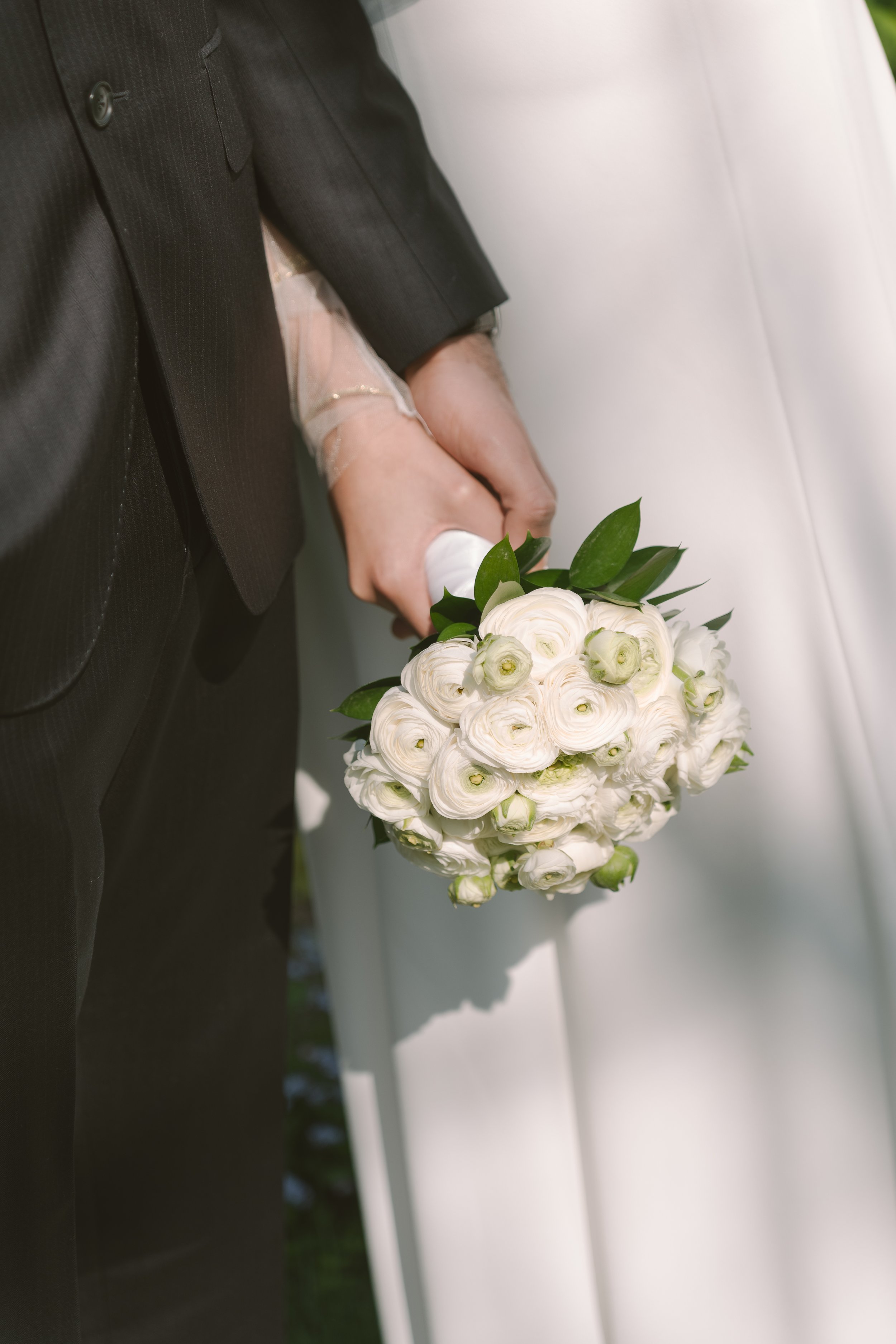 Un couple lors d'un mariage, la main de la personne portant un bouquet de fleurs blanches et la robe blanche de la mariée visible en arrière-plan.