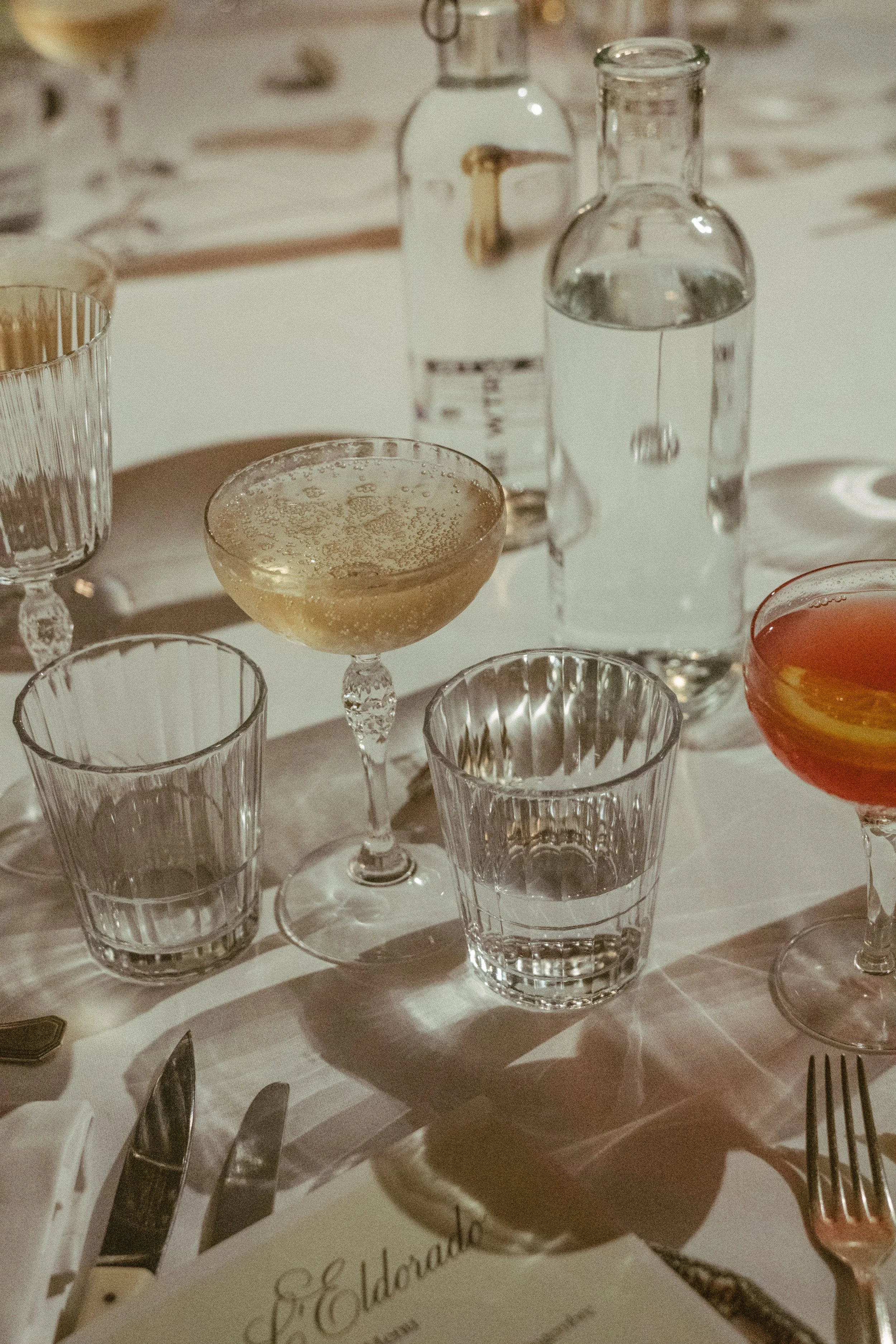 Verres et bouteilles d'eau sur une table, décorée pour un repas, avec un menu en français visible.