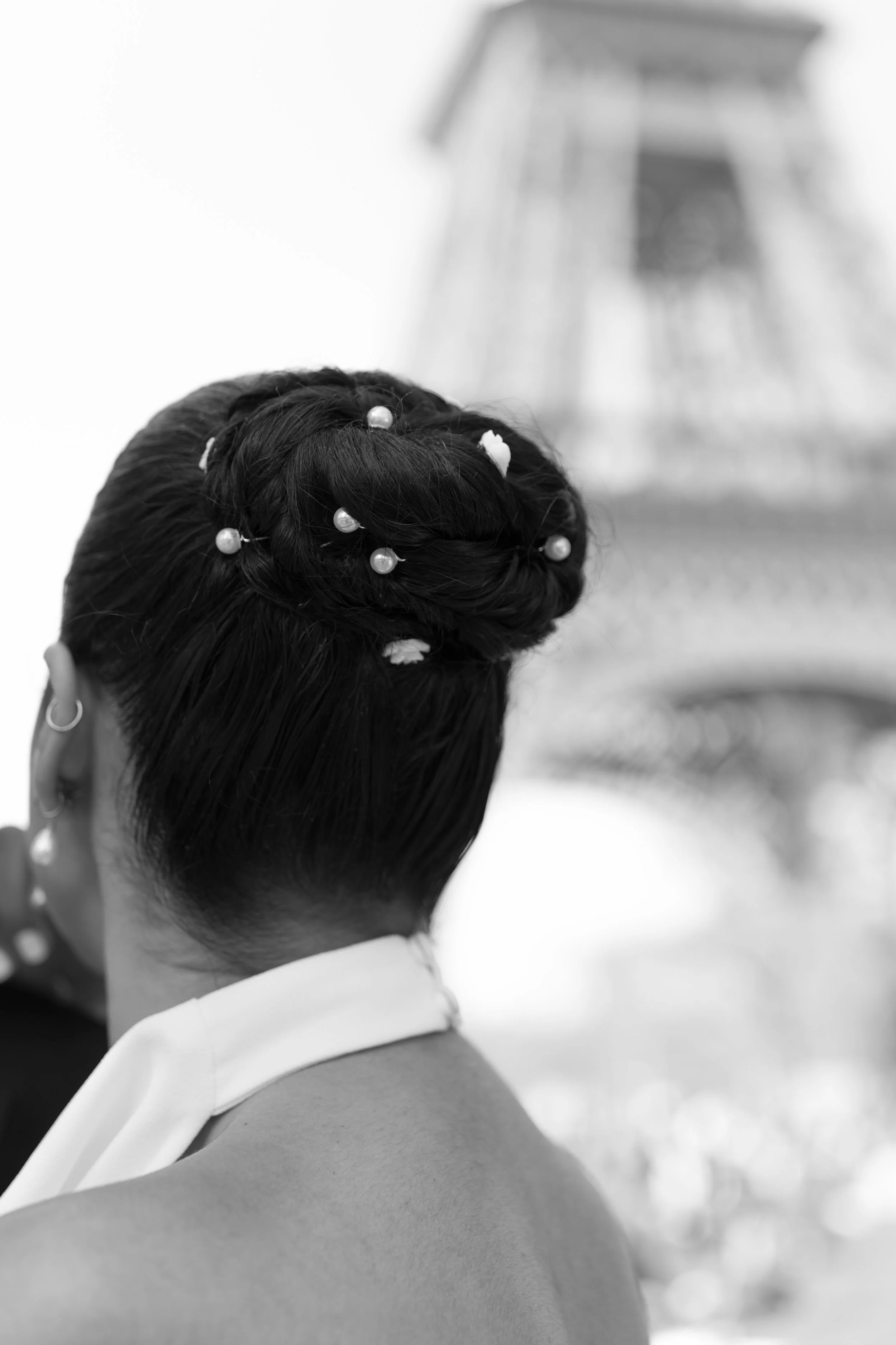 Coiffure sophistiquée avec perles et accessoires, vue de derrière, avec la Tour Eiffel floue en arrière-plan.
