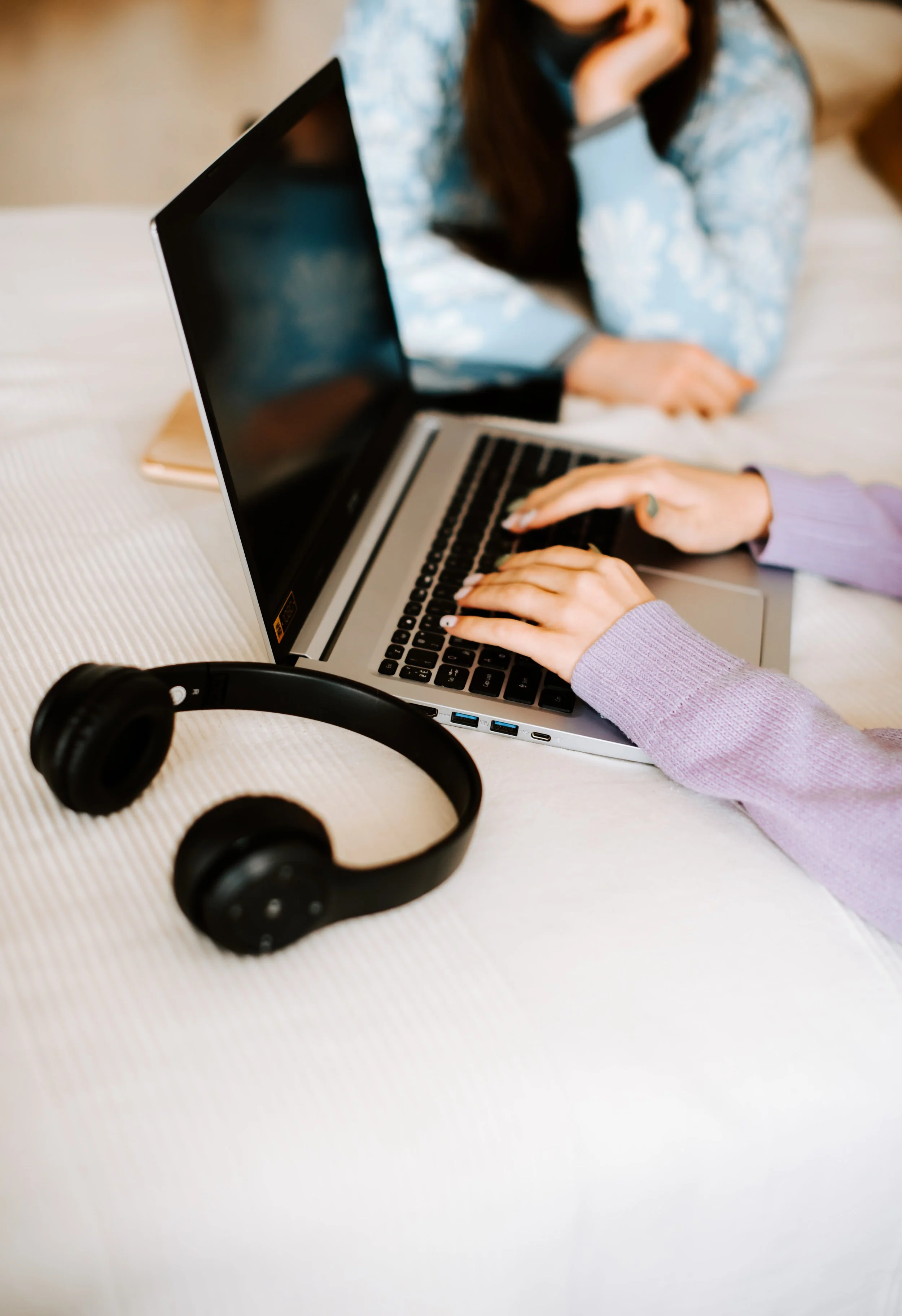 Deux personnes utilisent un ordinateur portable sur une table, avec un casque audio noir à côté.